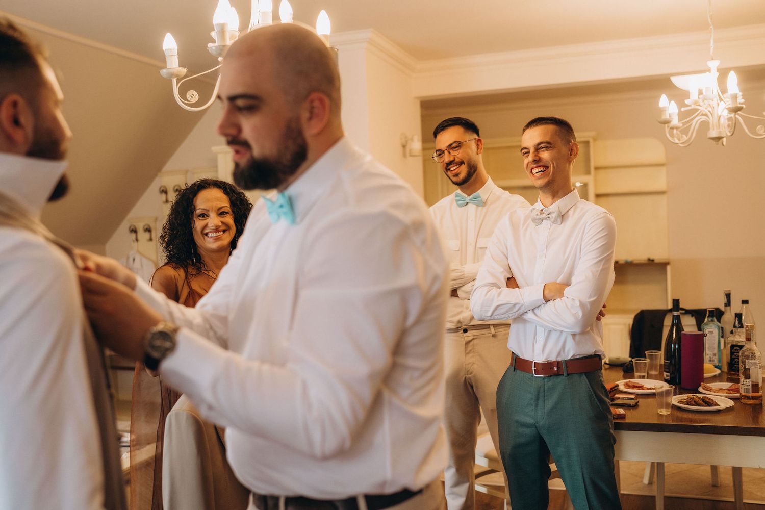 Groomsmen in white shirts and teal bow ties laughing together while getting ready for a wedding ceremony.