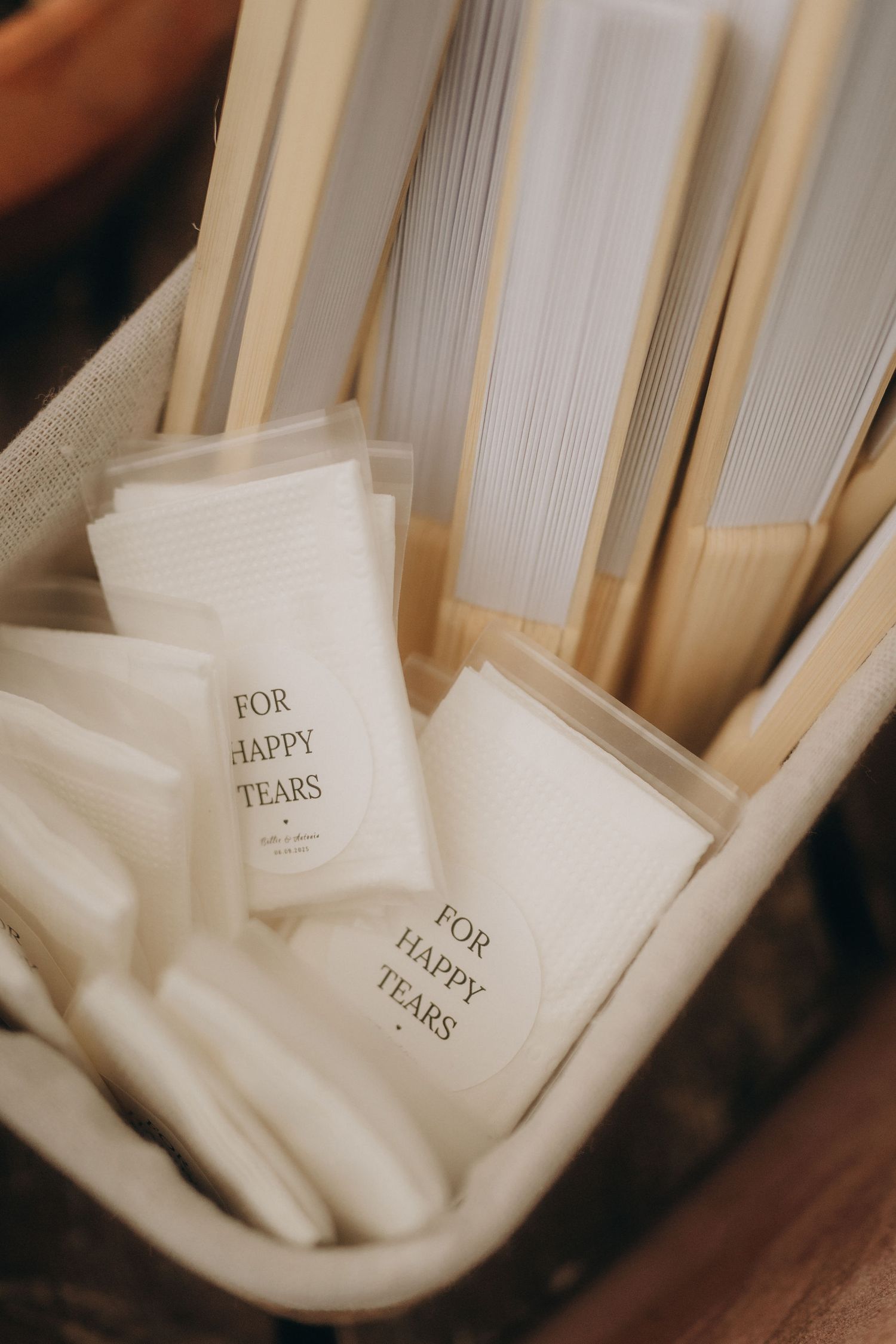 Basket of folded paper fans and "For Happy Tears" tissue packets, perfect wedding ceremony accessories.