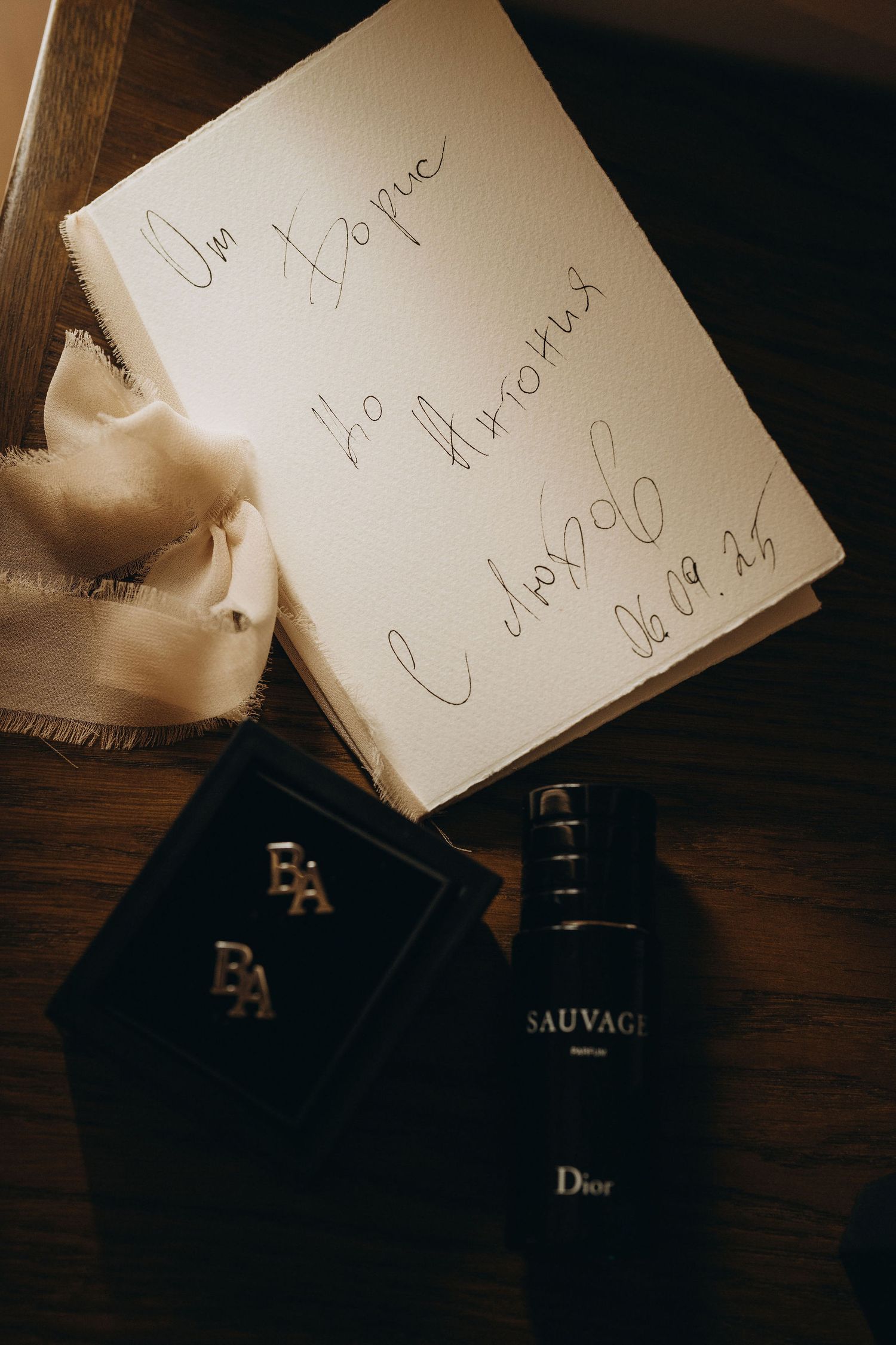 Dior Sauvage parfum bottle beside a jewelry box and handwritten note on a wooden surface.