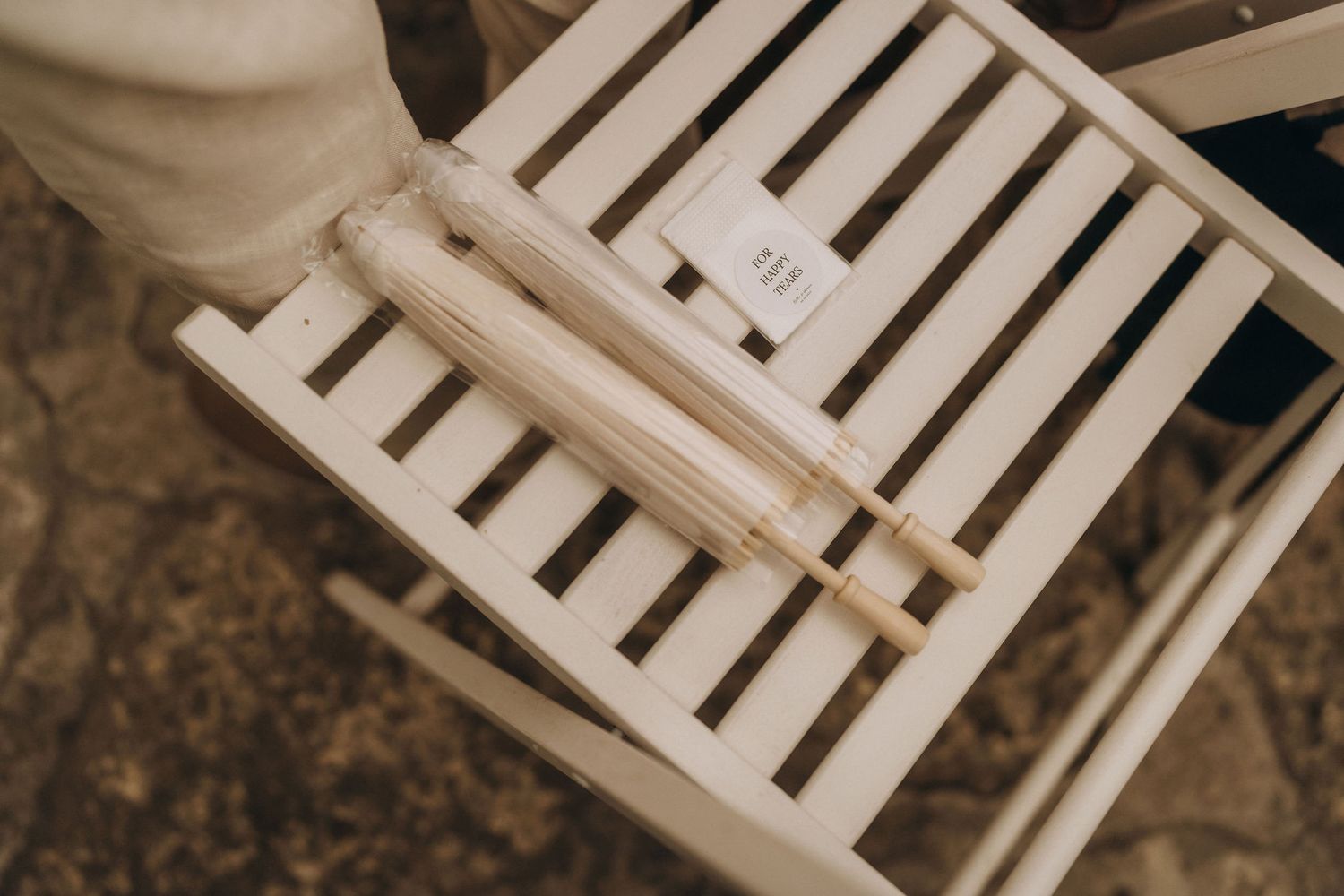 White folded paper fan program resting on a white wooden chair at an outdoor wedding.