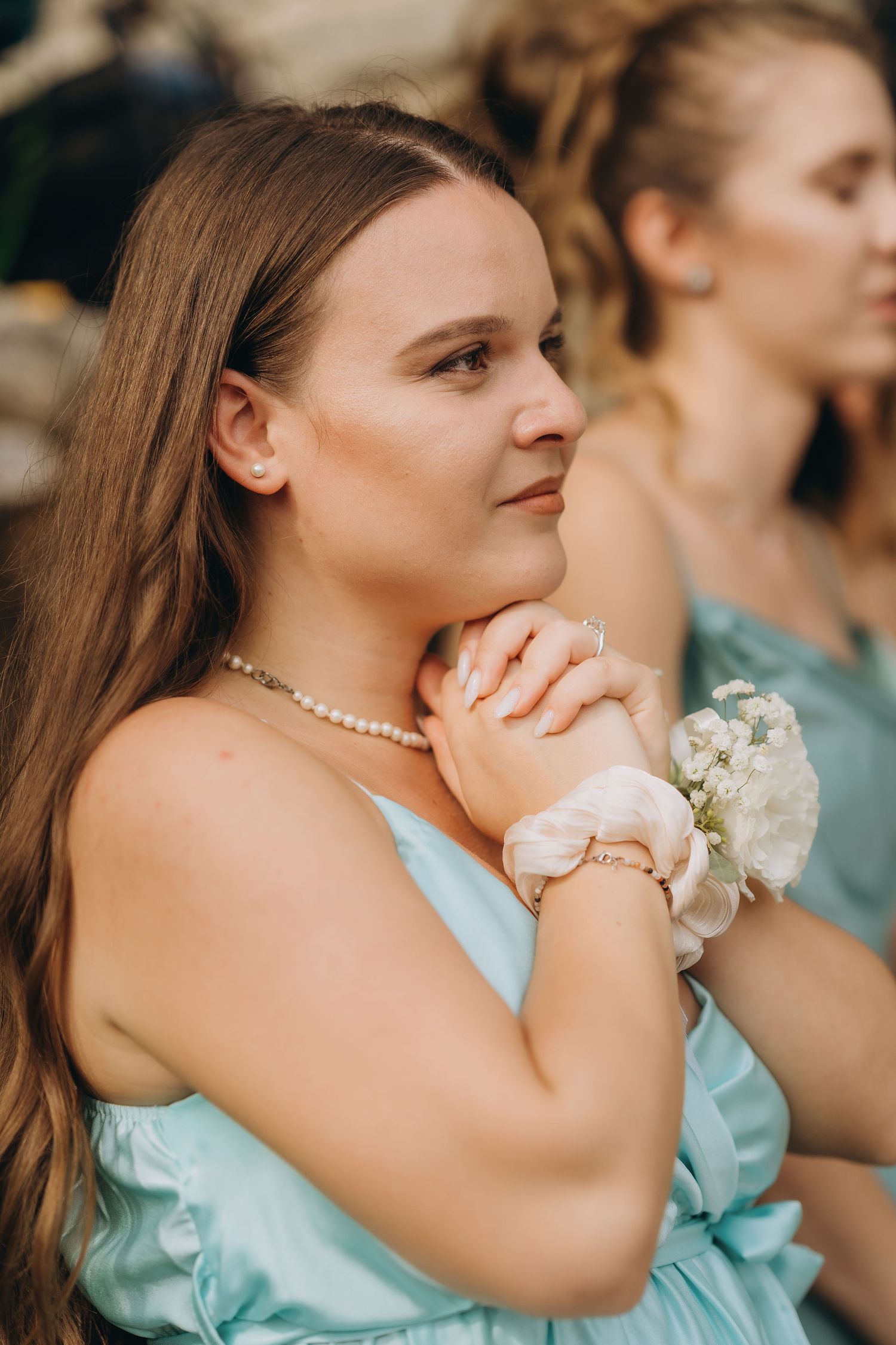 Young bridesmaid in mint dress with pearl necklace and floral wrist corsage at wedding ceremony.
