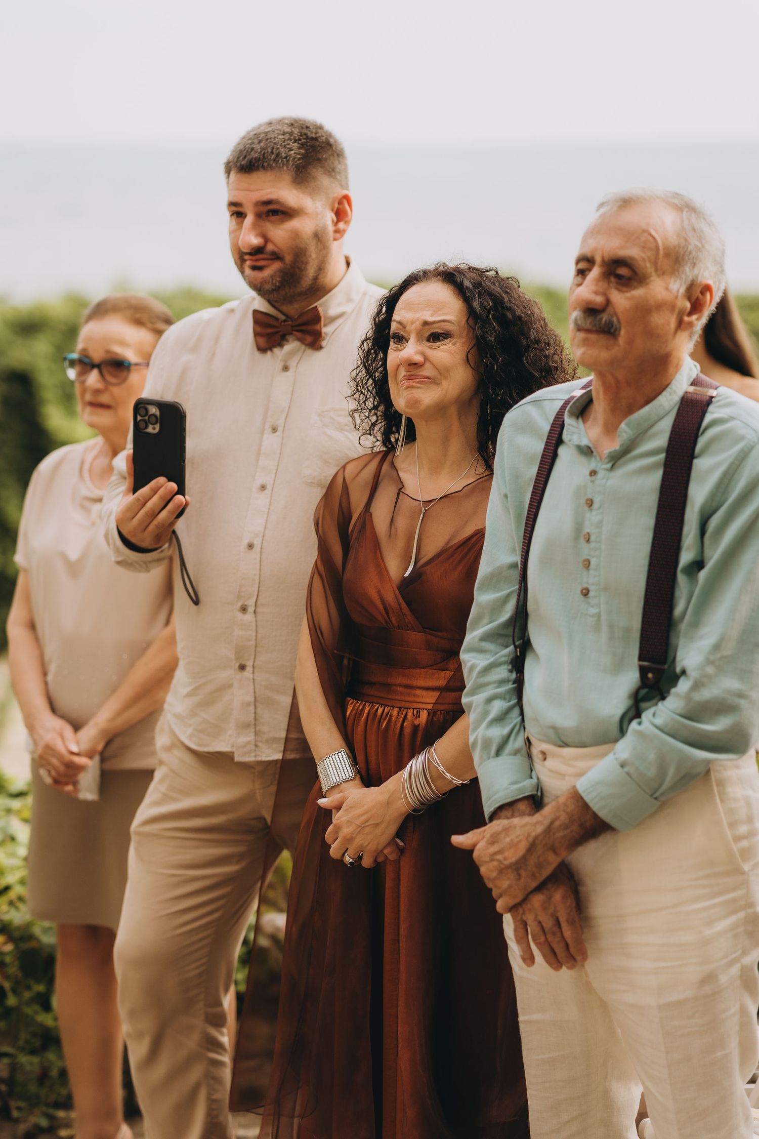 Group of elegantly dressed wedding guests posing for a selfie outdoors, wearing brown and neutral tones.