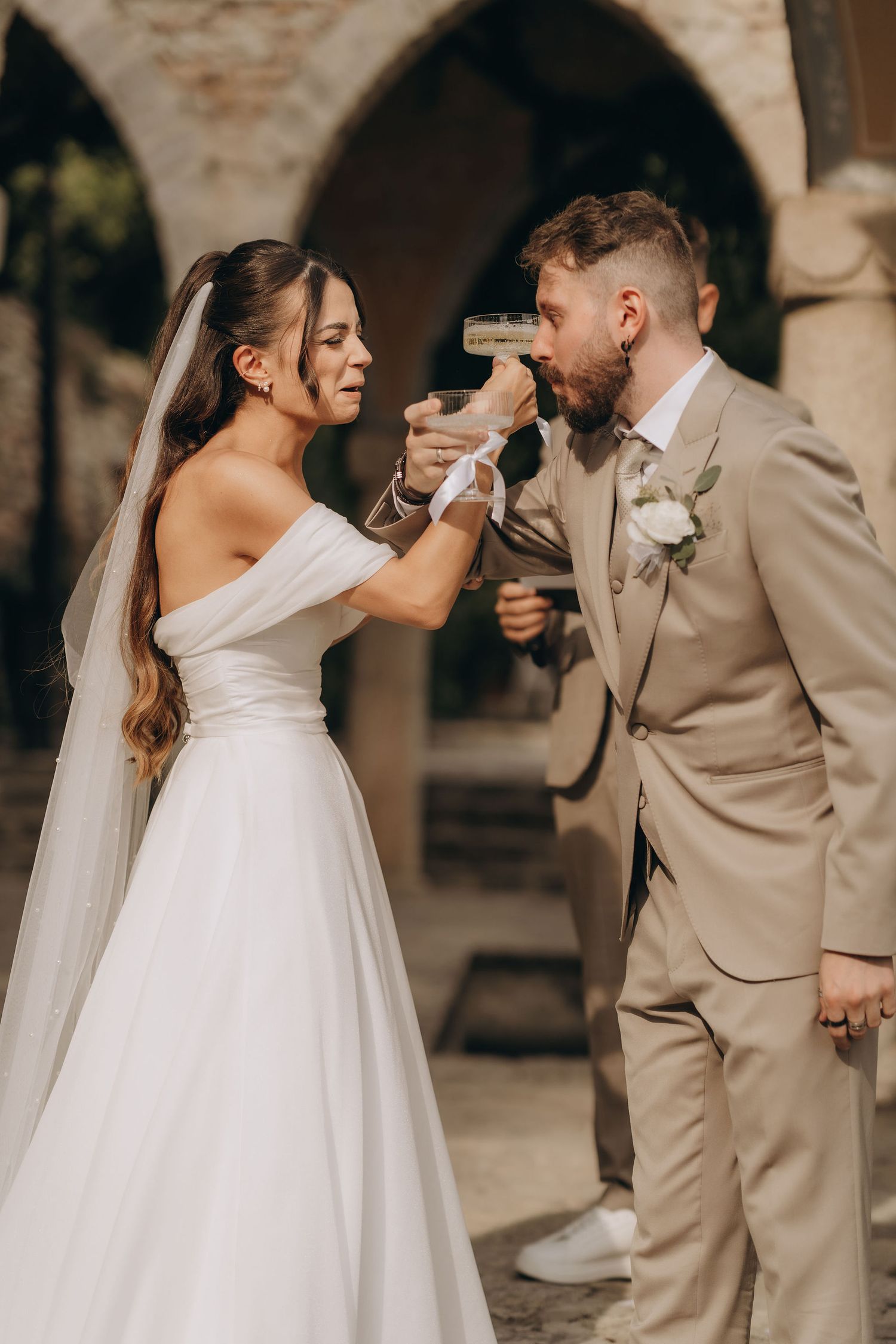 Bride and groom toasting with champagne glasses at their wedding, dressed in white gown and beige suit.