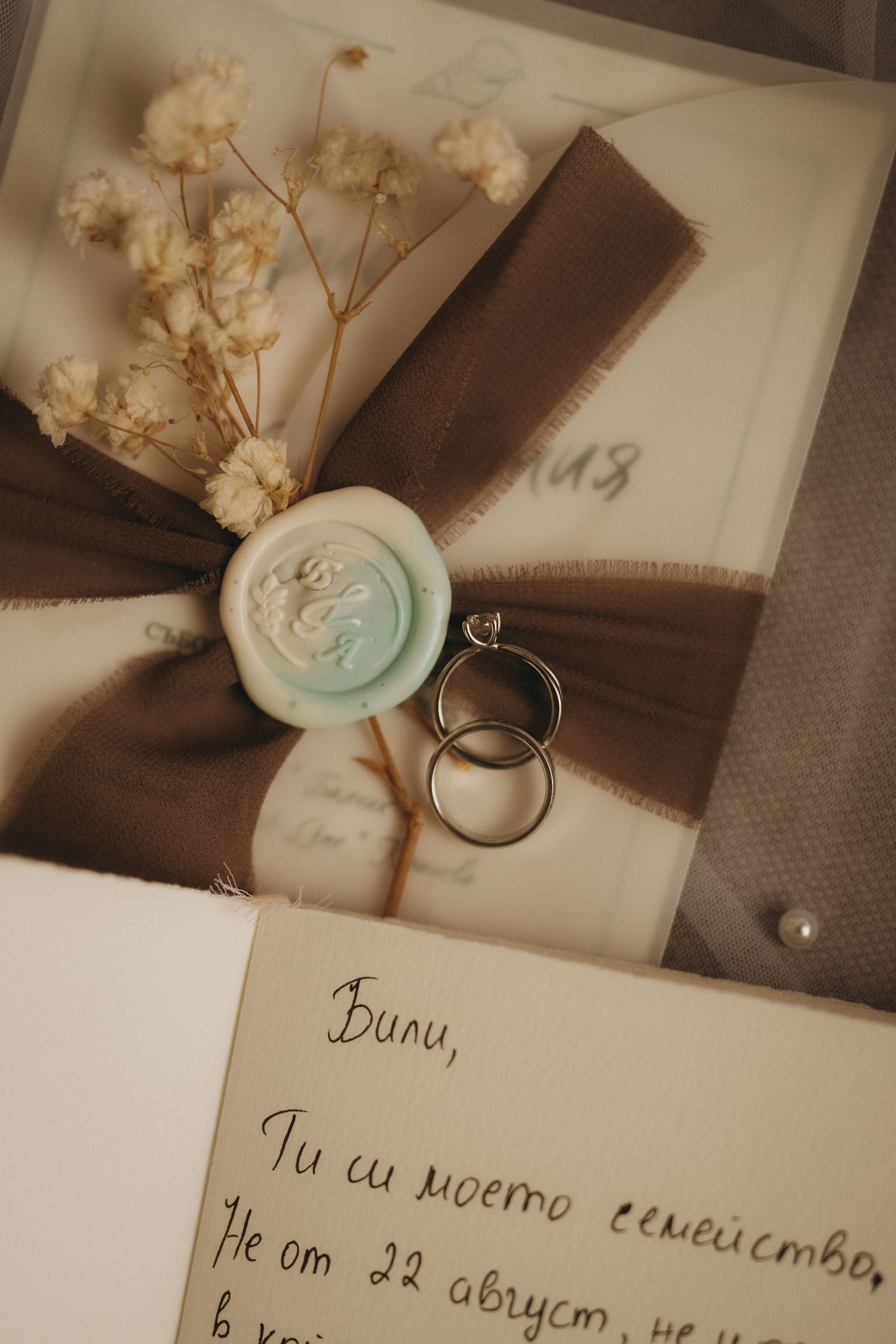 Elegant wedding invitation with two gold rings, wax seal, dried flowers, brown ribbon, and handwritten love letter in Bulgarian.