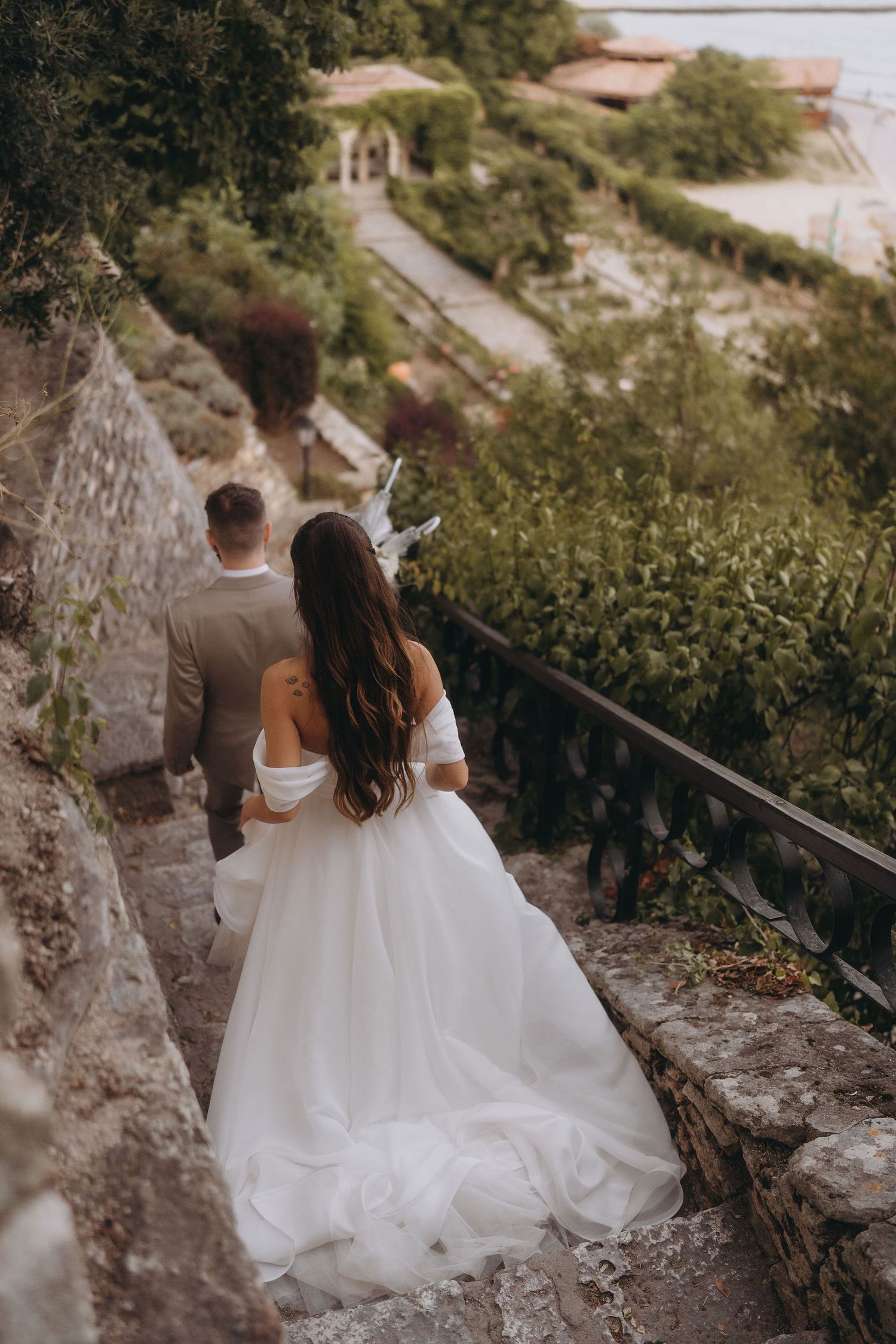 Bride and groom walking down stone steps surrounded by lush greenery at an outdoor wedding venue.