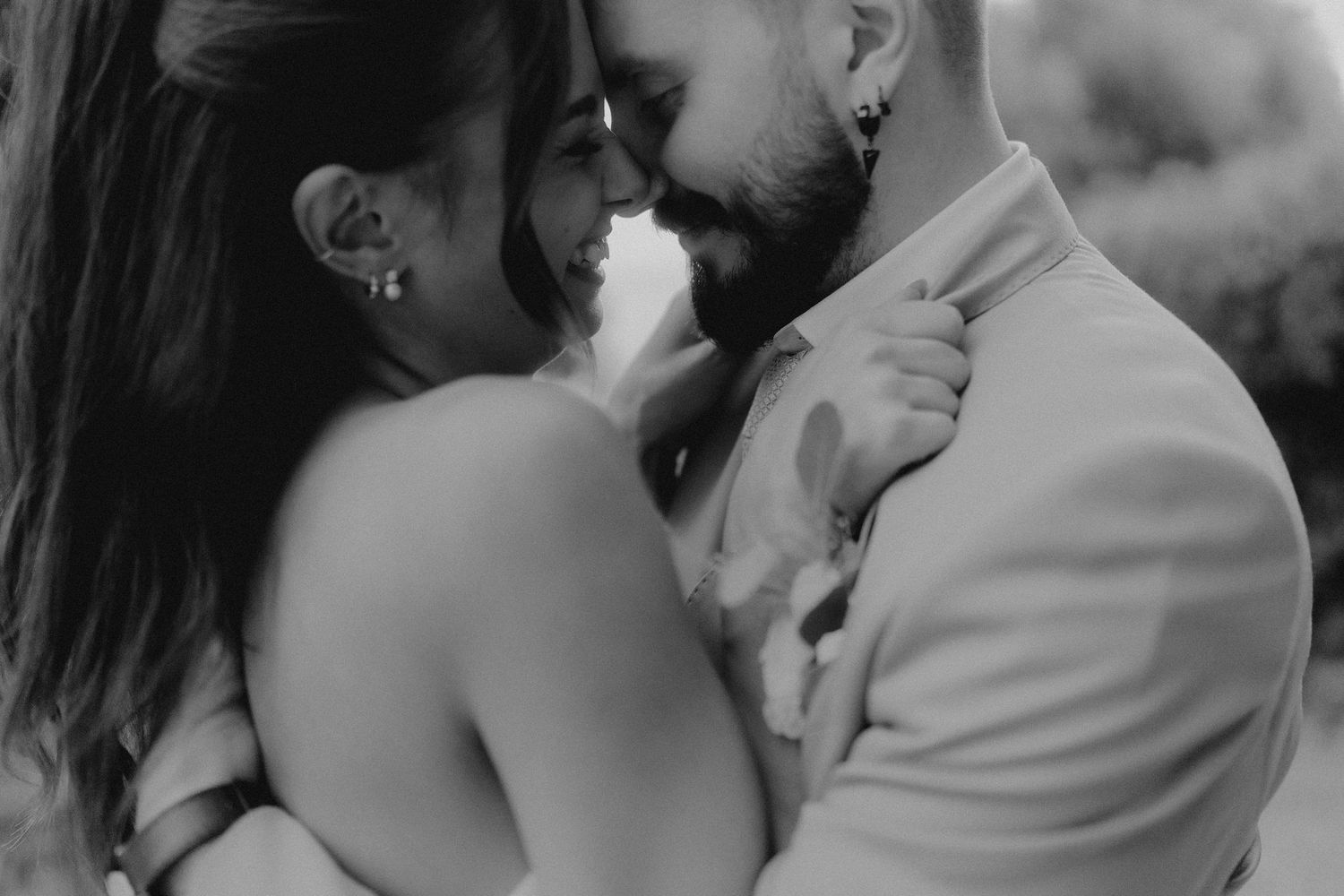 Black and white photo of a couple sharing an intimate romantic moment, nearly kissing at a wedding celebration.
