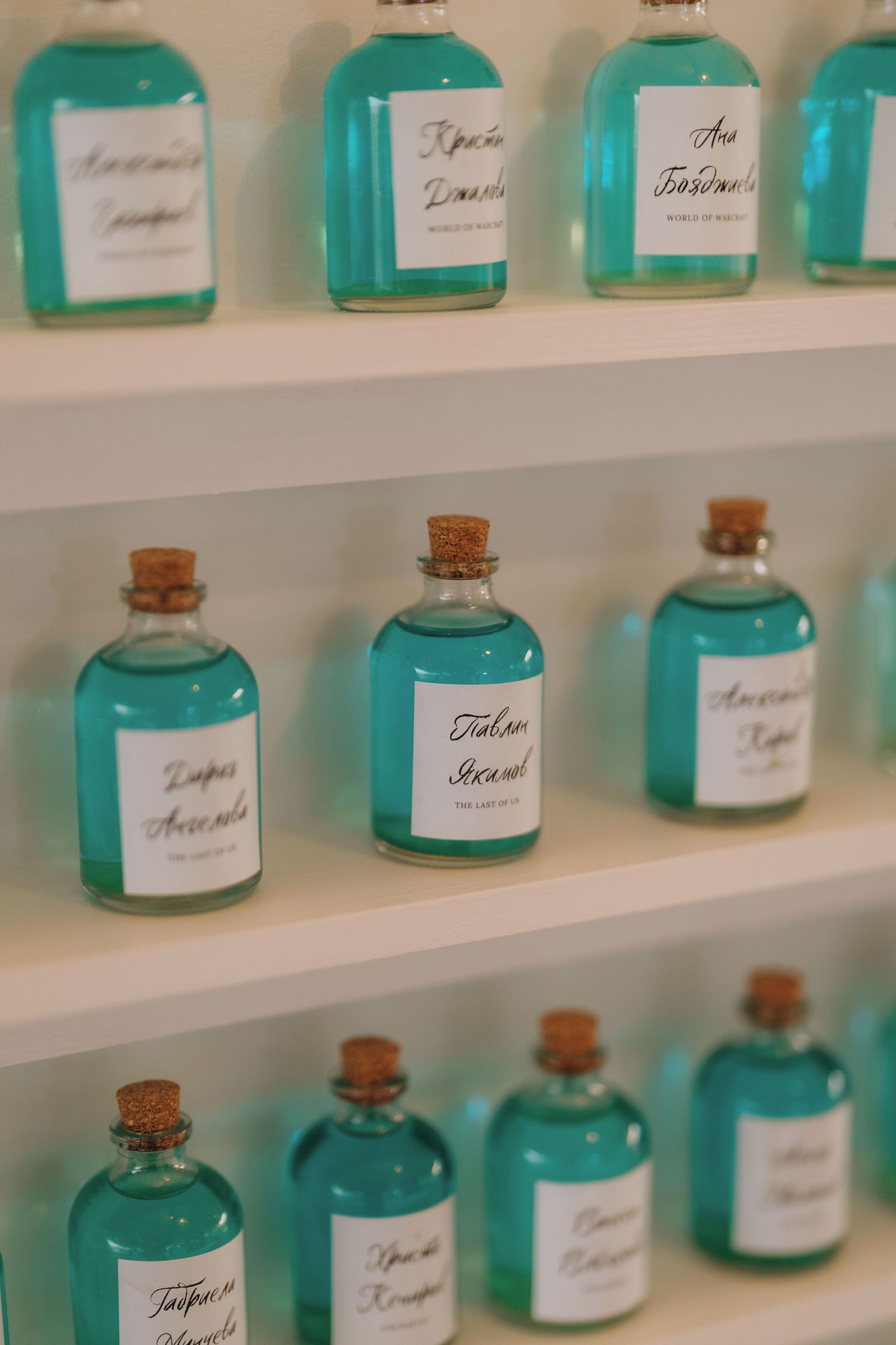 Teal blue liquid in small glass bottles with cork stoppers and handwritten labels displayed on white shelves.