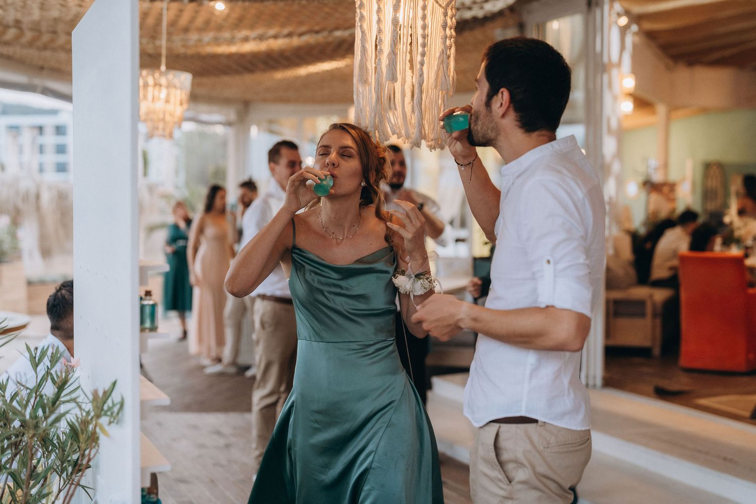 Elegant couple drinking from teal cups at an outdoor wedding reception in a decorated venue.