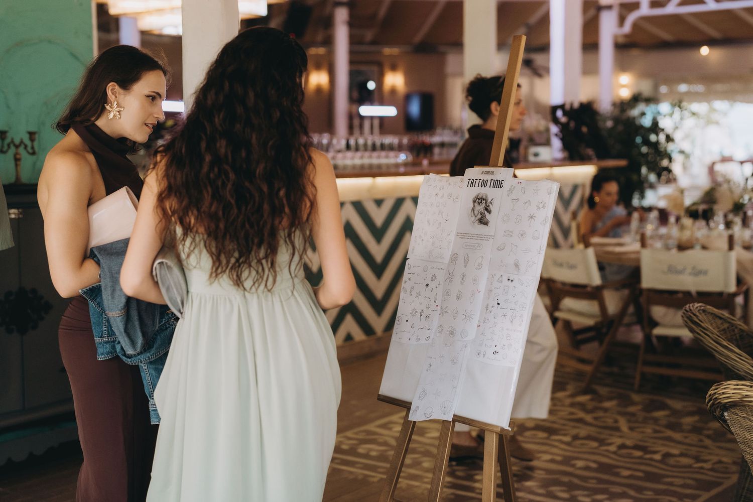 Two women reviewing a seating chart on an easel at an elegant wedding reception venue.