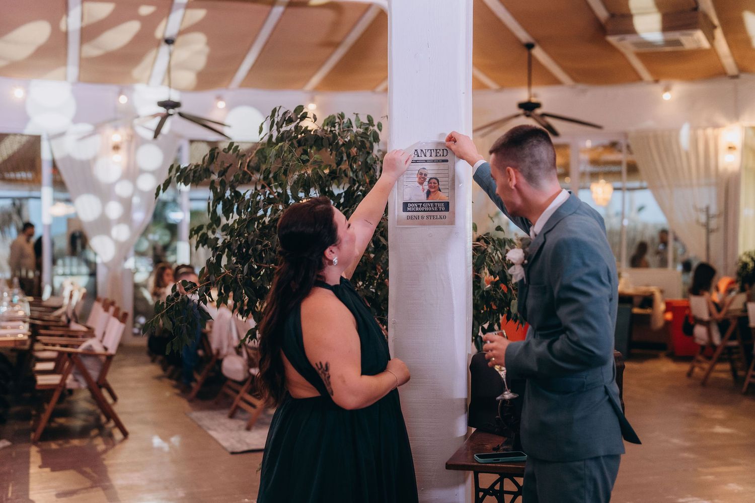 Couple reading a posted notice on a pillar at a decorated indoor wedding reception venue.