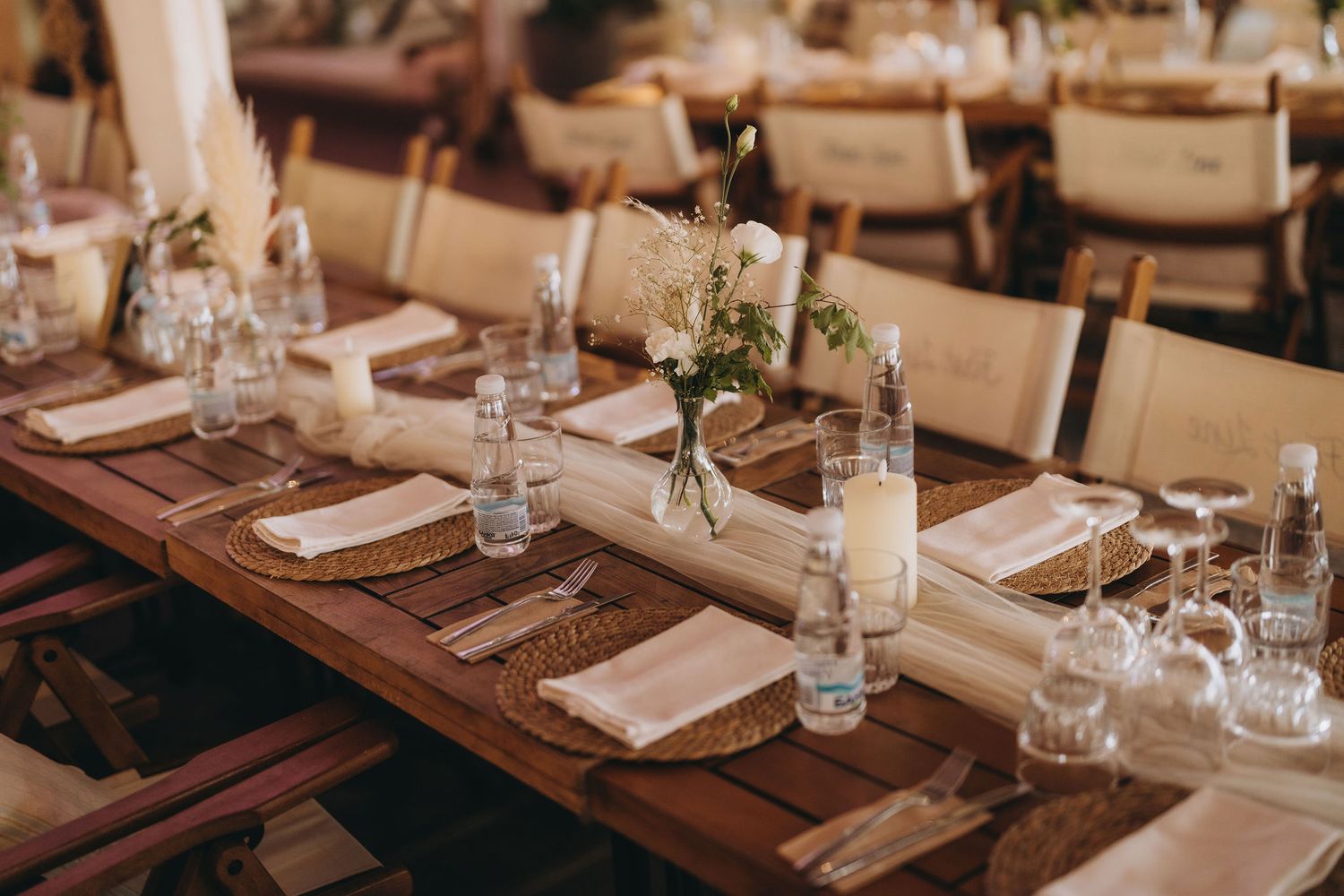 Elegant rustic wedding reception table set with linen napkins, glassware, candles, and floral centerpieces on wooden tables.