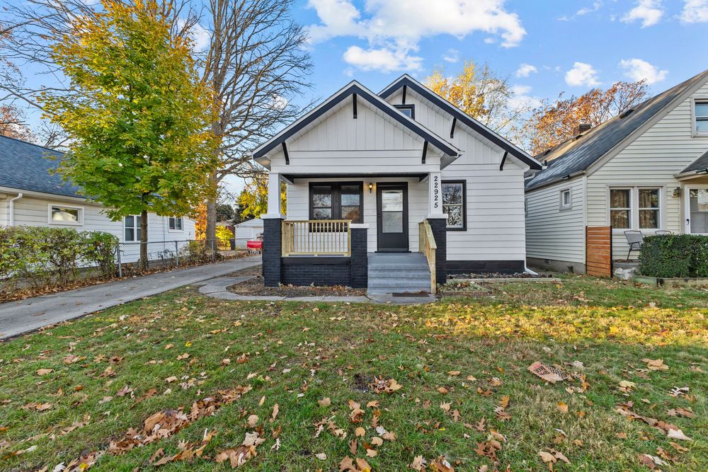Charming white bungalow with black trim, covered porch, and colorful autumn trees in a well-maintained front yard.