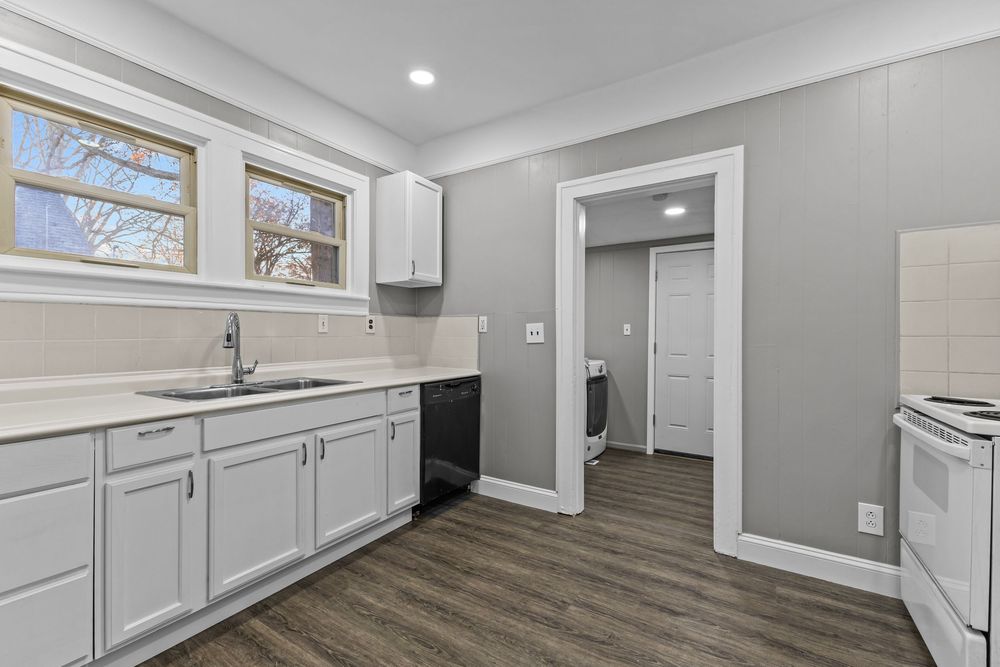 Modern kitchen with white cabinets, dark hardwood floors, black dishwasher, white range, and a window above the sink.