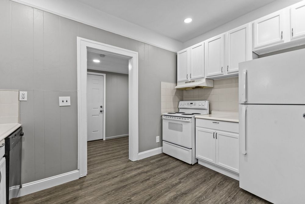 White kitchen with white appliances, white cabinets, gray walls, and dark hardwood floors leading to a hallway.