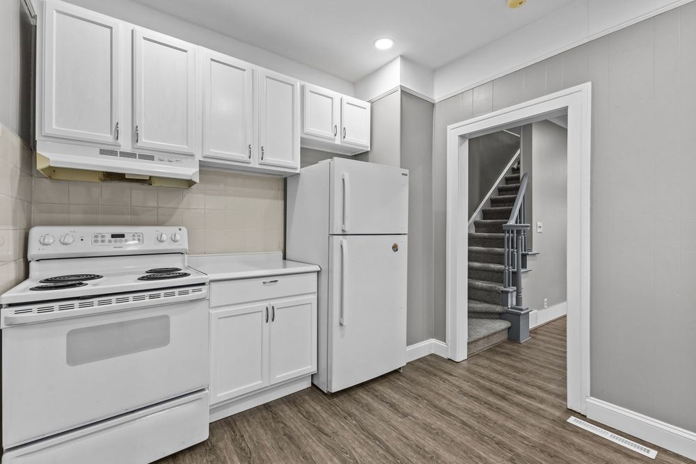 Modern kitchen with white cabinets, white appliances, and dark hardwood floors in a clean layout.