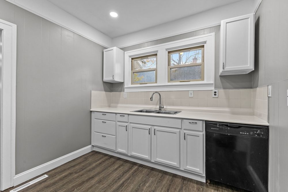 Modern kitchen with white cabinets, black dishwasher, undermount sink, and dark hardwood floors.