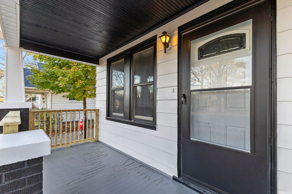 Dark front door with glass panels on a covered porch with white siding and wood deck flooring.