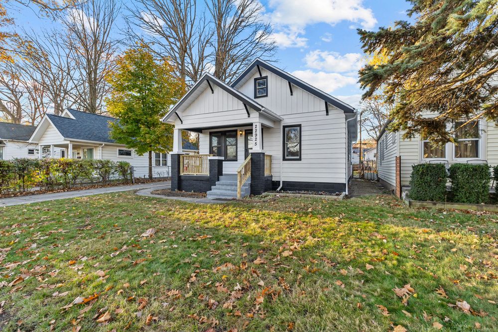 Charming bungalow home with gray siding, covered front porch, and lush green lawn surrounded by mature trees in fall.