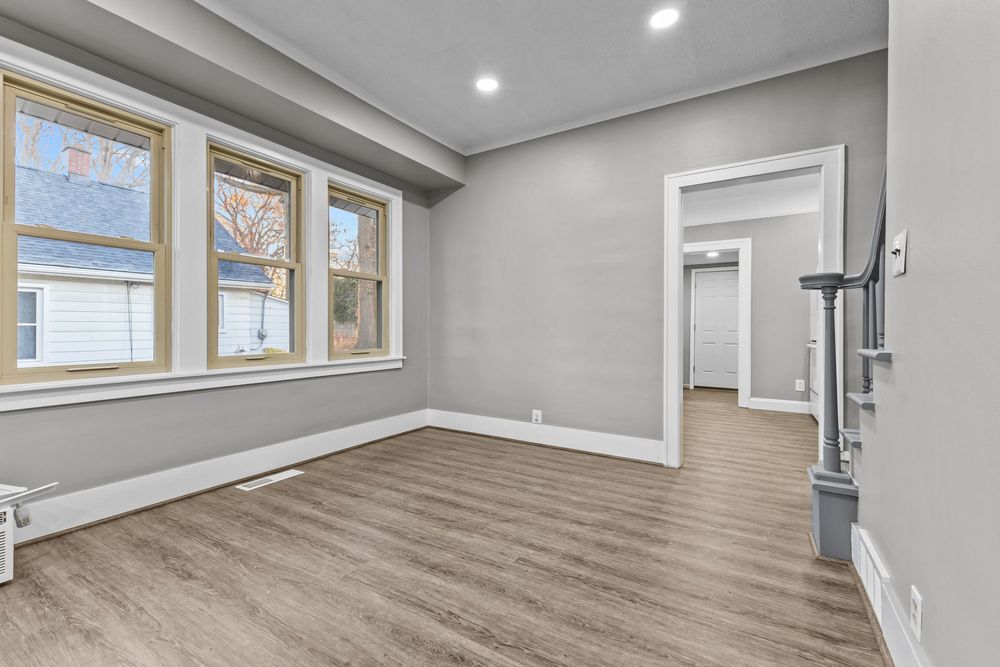 Bright empty room with gray walls, luxury vinyl plank flooring, white trim, and large windows allowing natural light.
