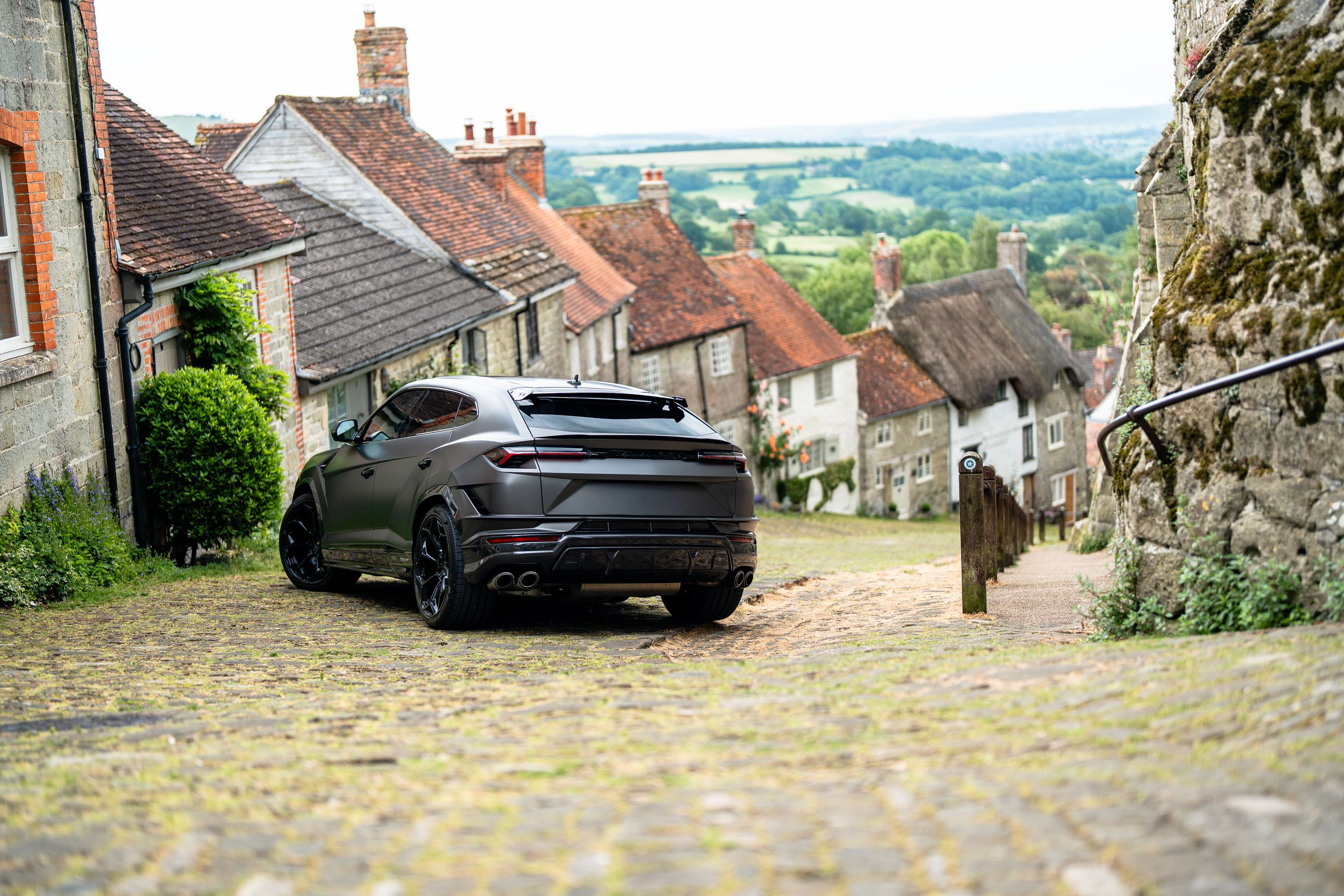 Matte black Lamborghini Urus SUV parked on cobblestone Gold Hill street in Shaftesbury, England.