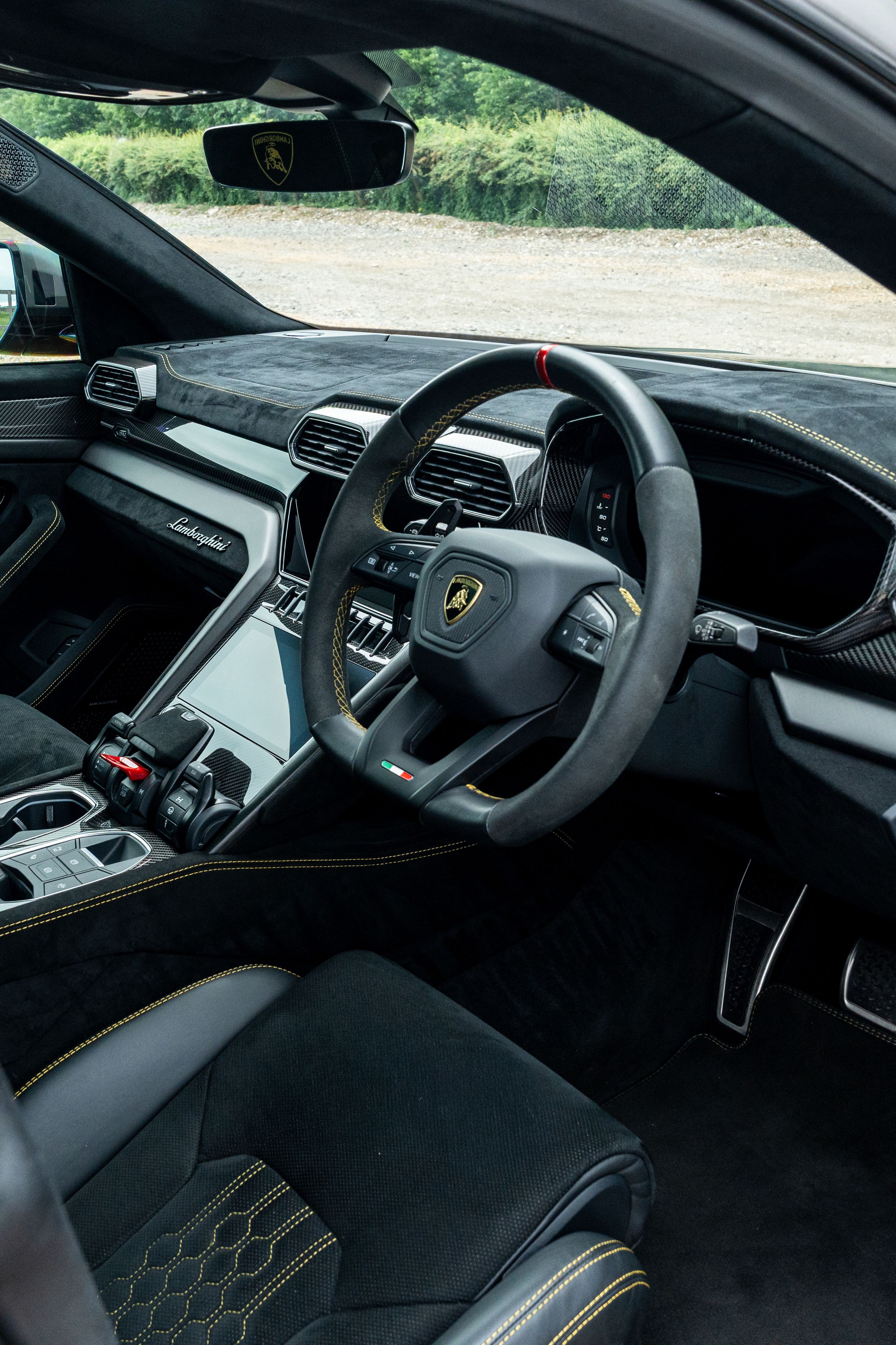 Lamborghini Urus interior featuring carbon fiber dashboard, Alcantara steering wheel, and sport seats in right-hand drive configuration.