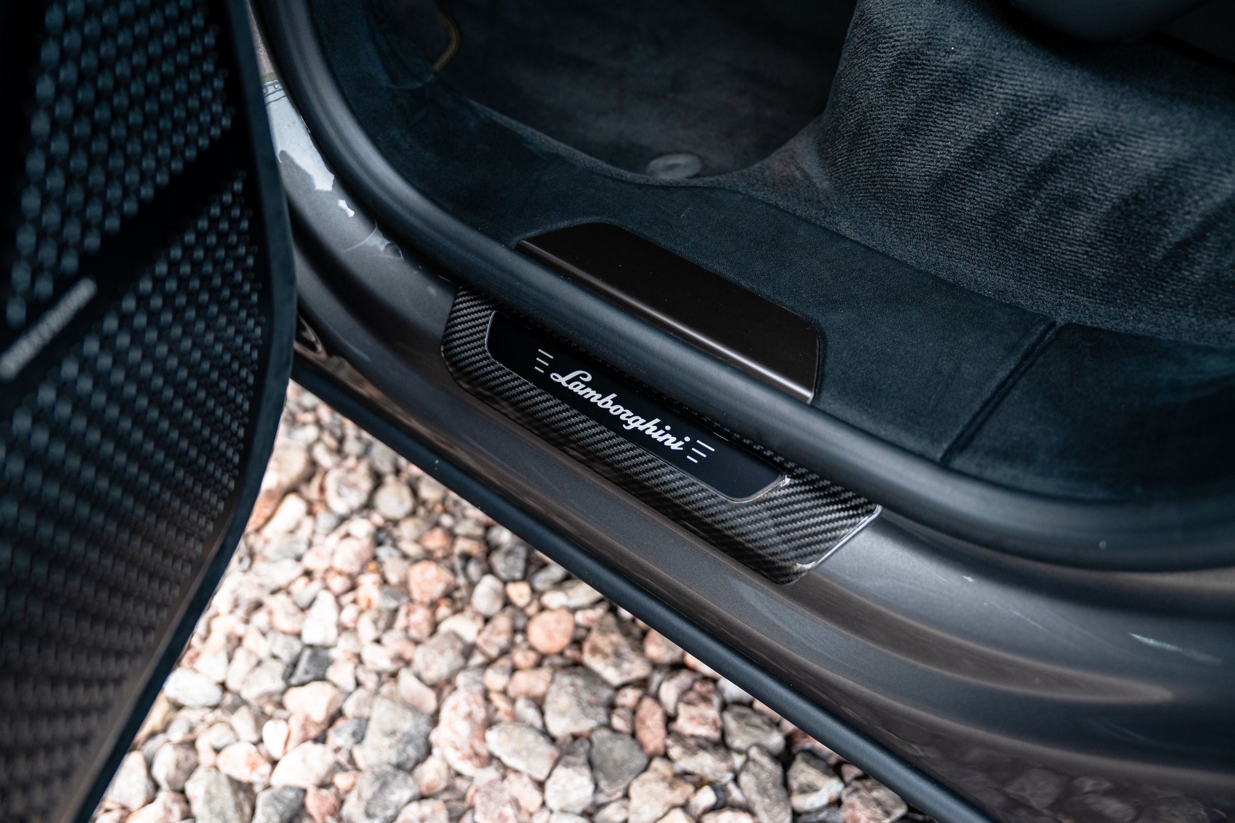 Lamborghini carbon fiber door sill plate with illuminated logo on a luxury sports car interior.
