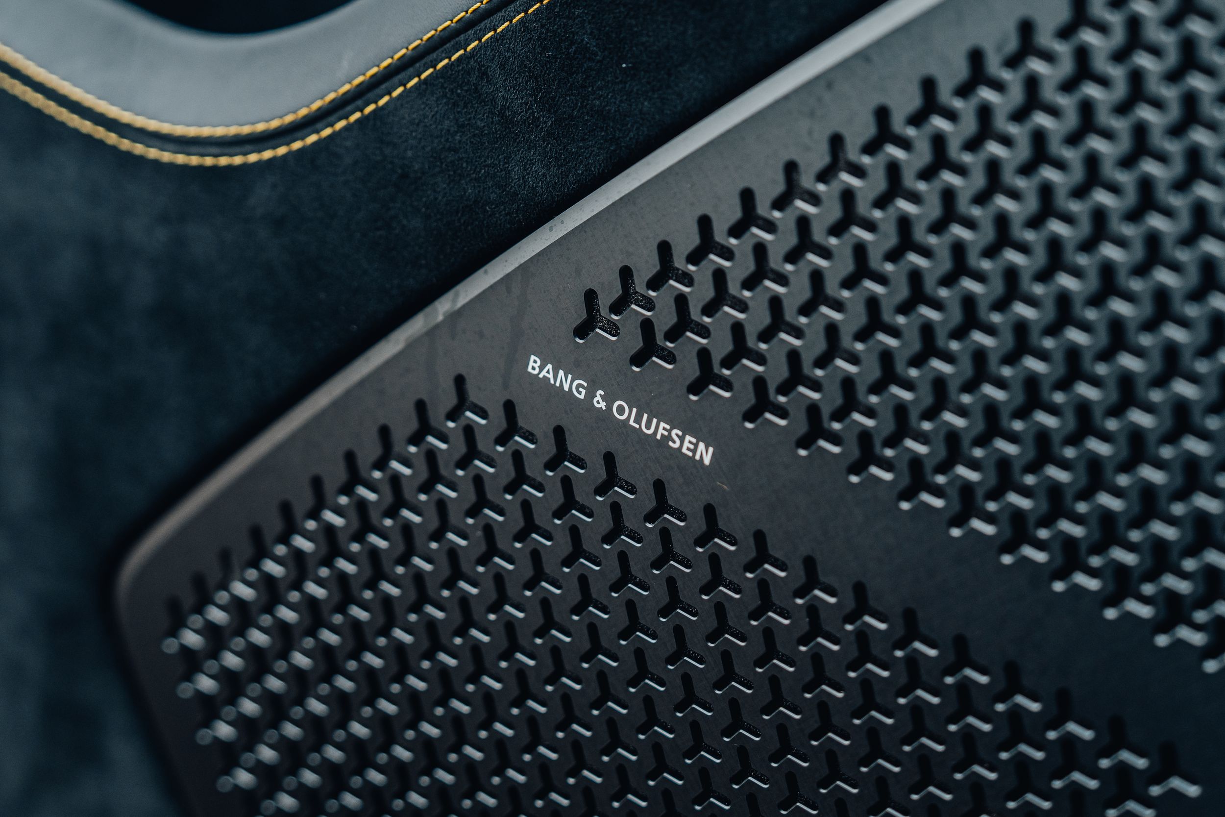 Close-up of a Bang & Olufsen speaker grille in a luxury car interior with textured black surface.