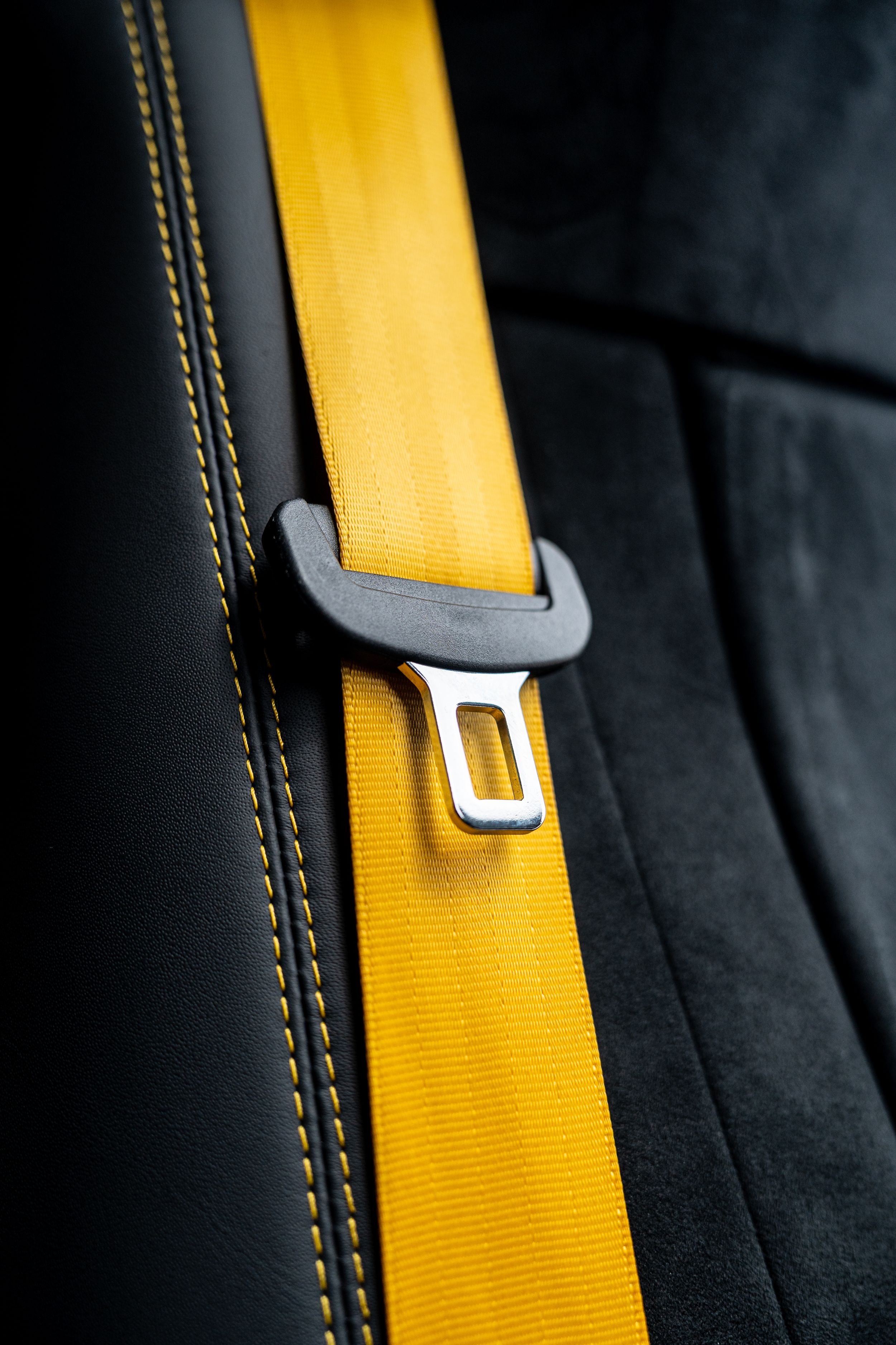Close-up of a yellow seatbelt buckled against black leather car seat with yellow stitching detail.