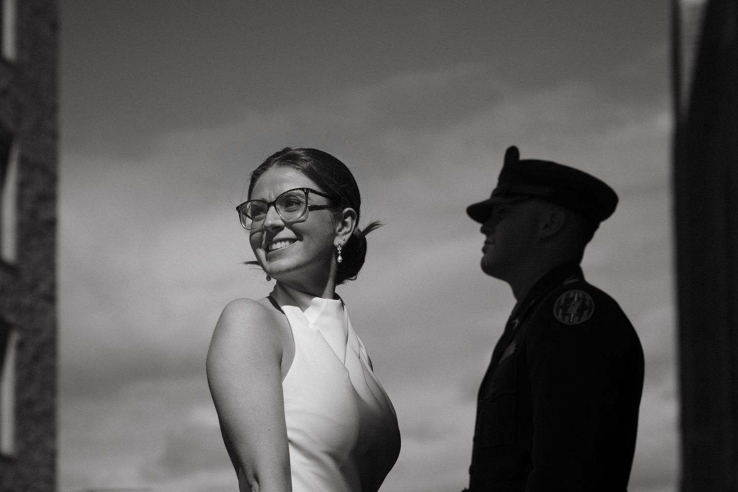 Black and white photo of a smiling woman in white dress with a military officer in uniform outdoors.