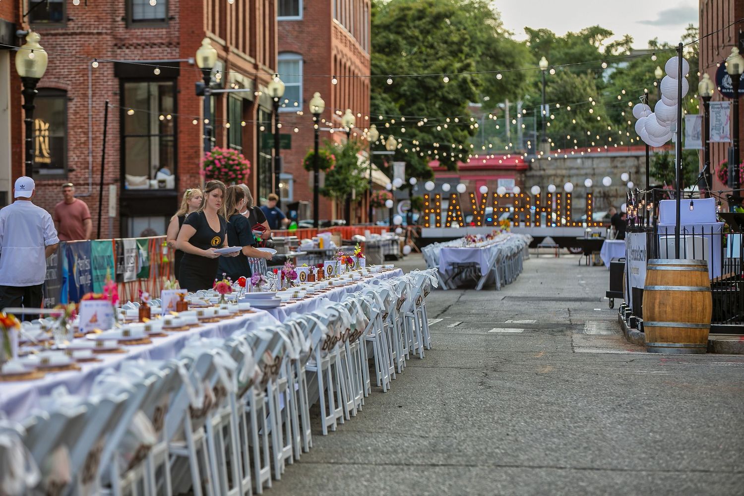 Long outdoor dining tables set up on a city street with string lights for an evening al fresco event.