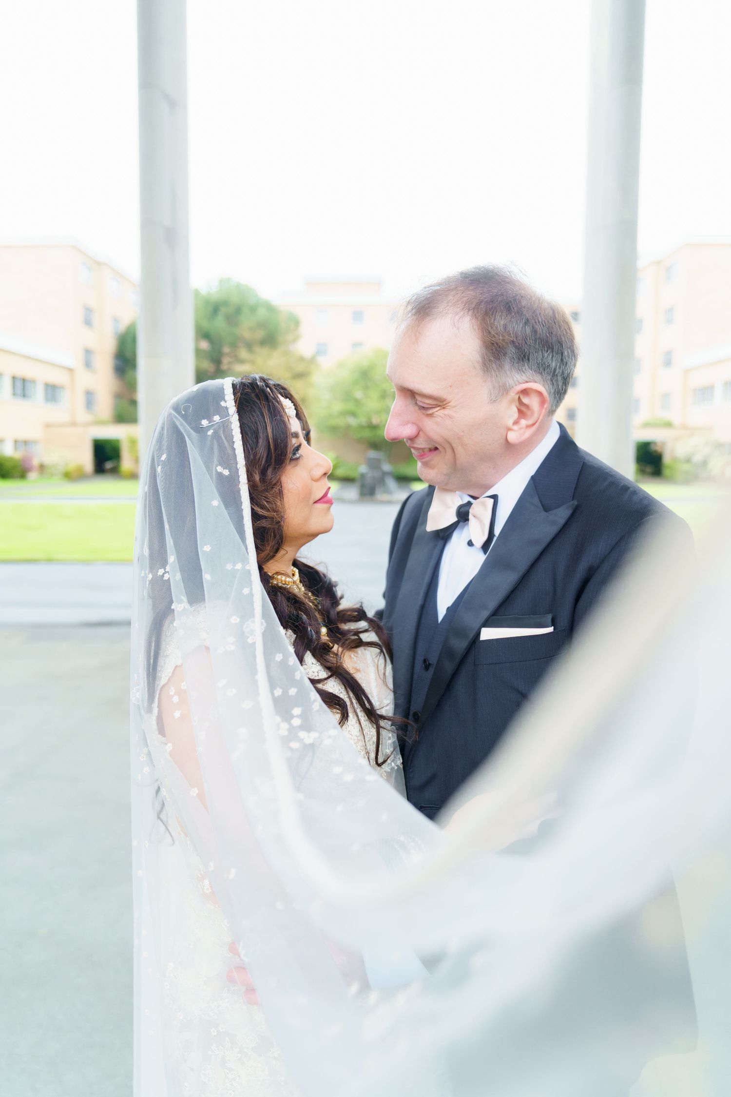 Couple in a greenhouse, groom in tan suit kissing bride wearing a red traditional Indian bridal saree.