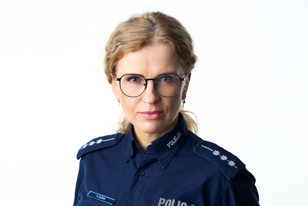 Female police officer in dark blue uniform with glasses poses for professional portrait photo against white background.