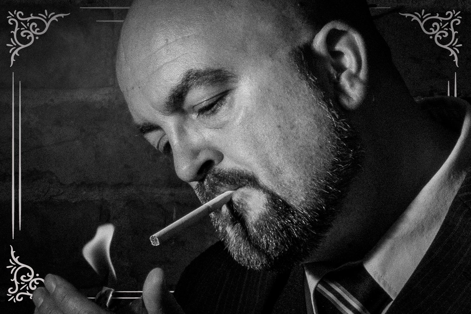 Black and white portrait of a bald man with beard lighting a cigarette, dramatic noir style photography.