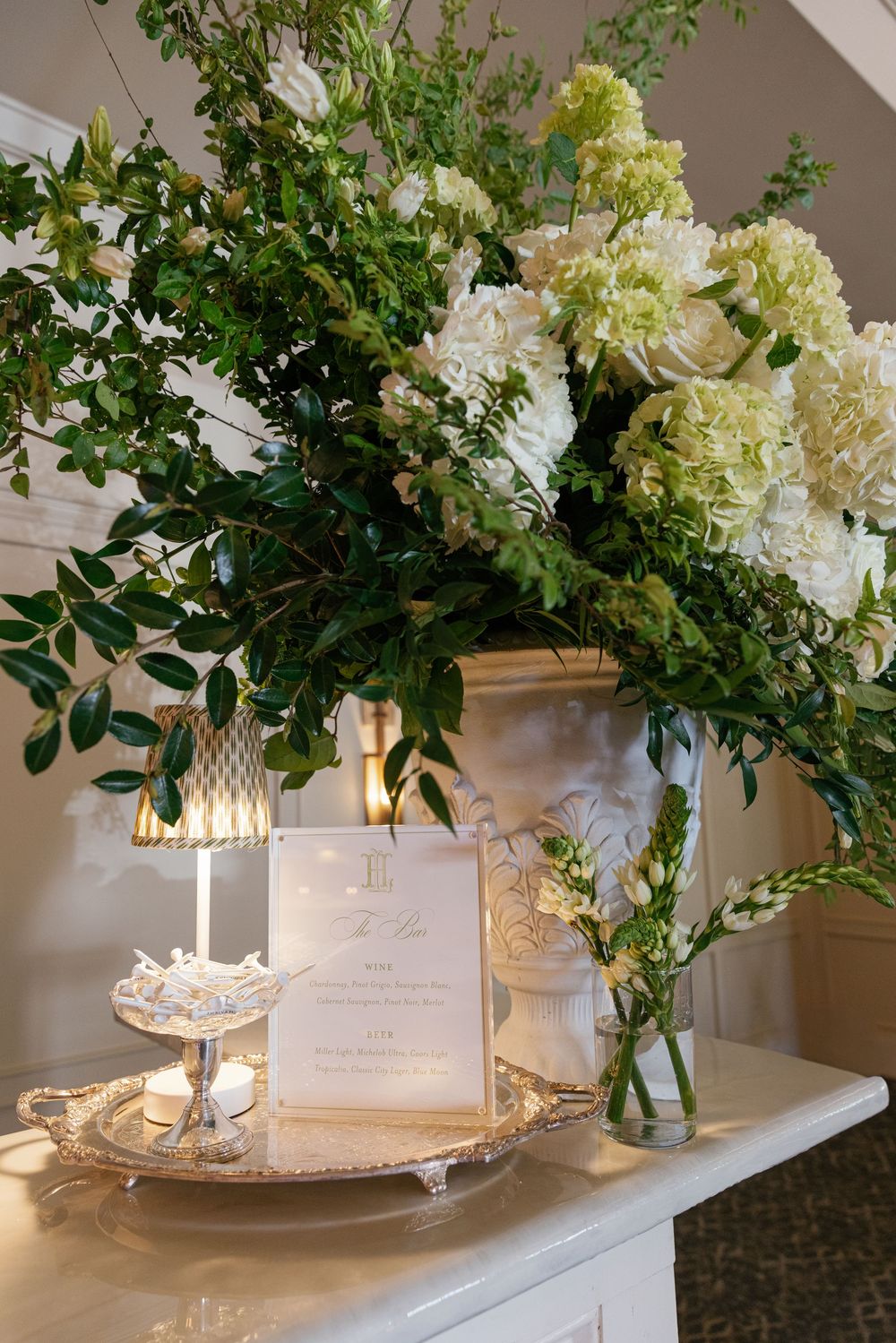 White floral wedding reception arrangement with hydrangeas, greenery, candles, and menu card.