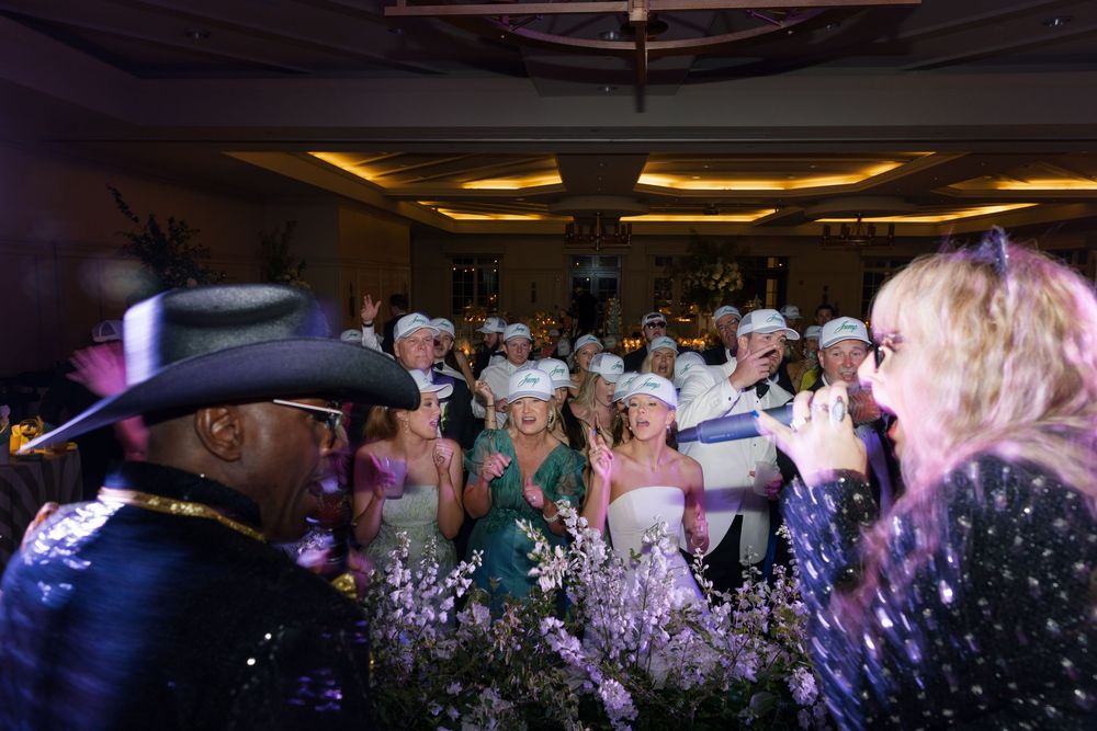 Lively wedding reception dance floor with guests celebrating around a floral centerpiece with confetti.