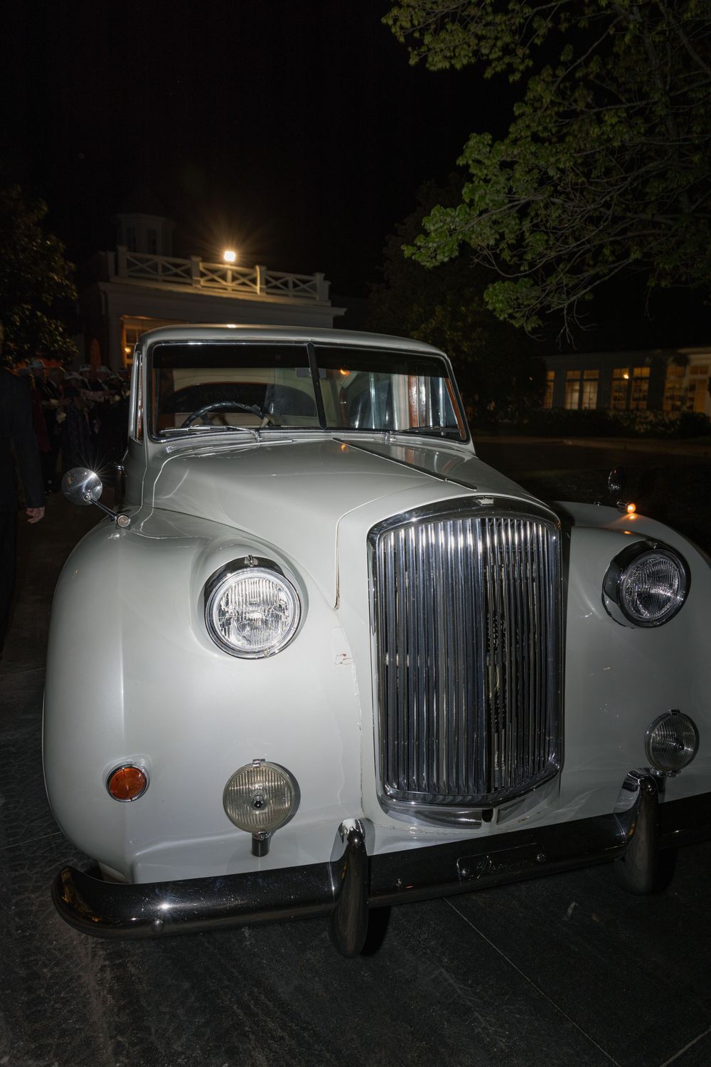 White vintage classic car parked at night outside an illuminated building.