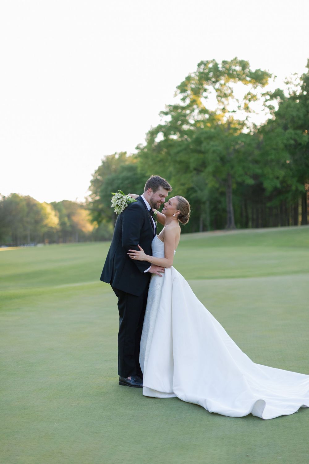 Bride and groom sharing a romantic kiss on a lush green golf course at sunset.
