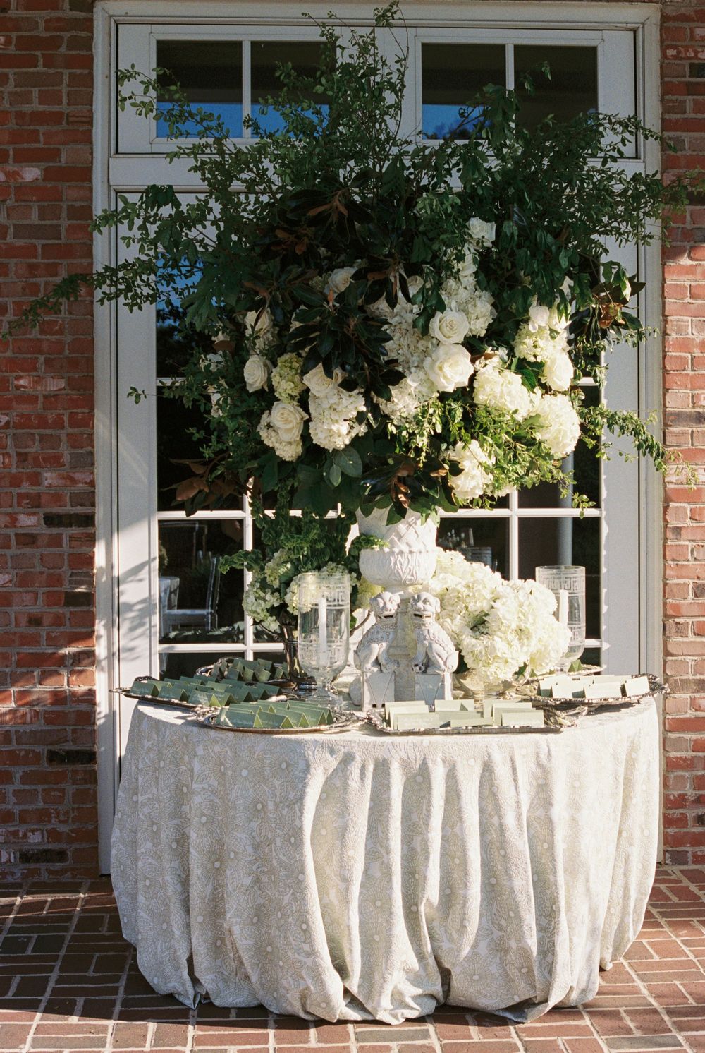Elegant wedding welcome table with white hydrangea floral arrangement outside brick building.