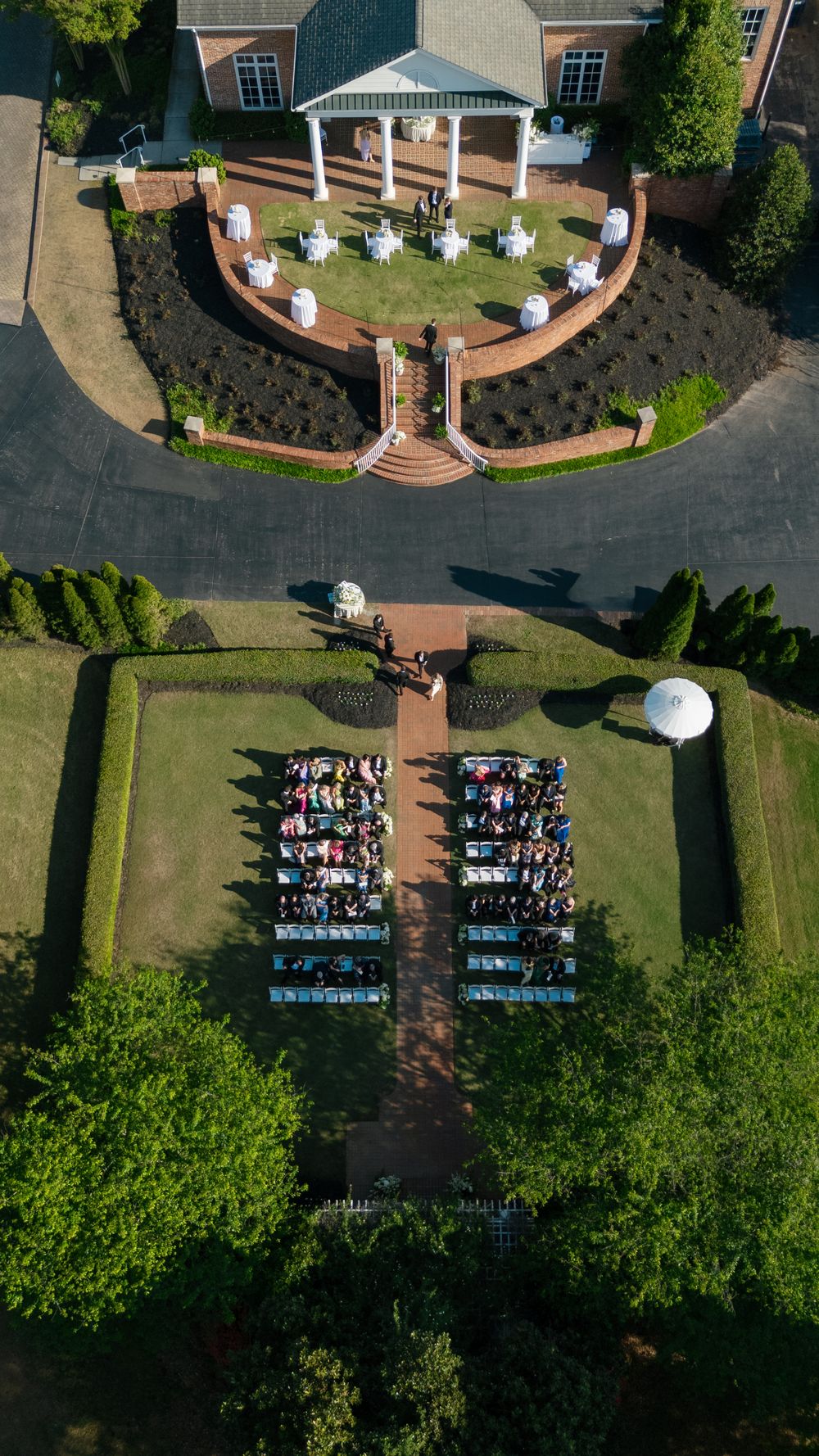 Aerial drone view of an outdoor wedding ceremony with guests seated in rows on a brick pathway.