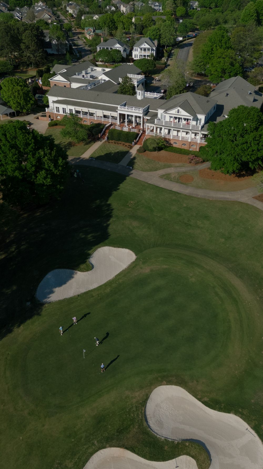 Aerial view of elegant golf club clubhouse surrounded by lush green fairways and sand bunkers.