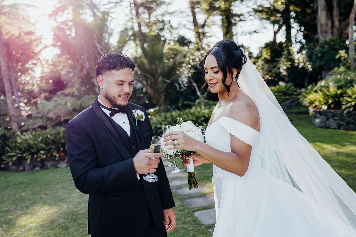 A couple in wedding attire poses in a sunlit garden during golden hour, creating a romantic and ethereal atmosphere.