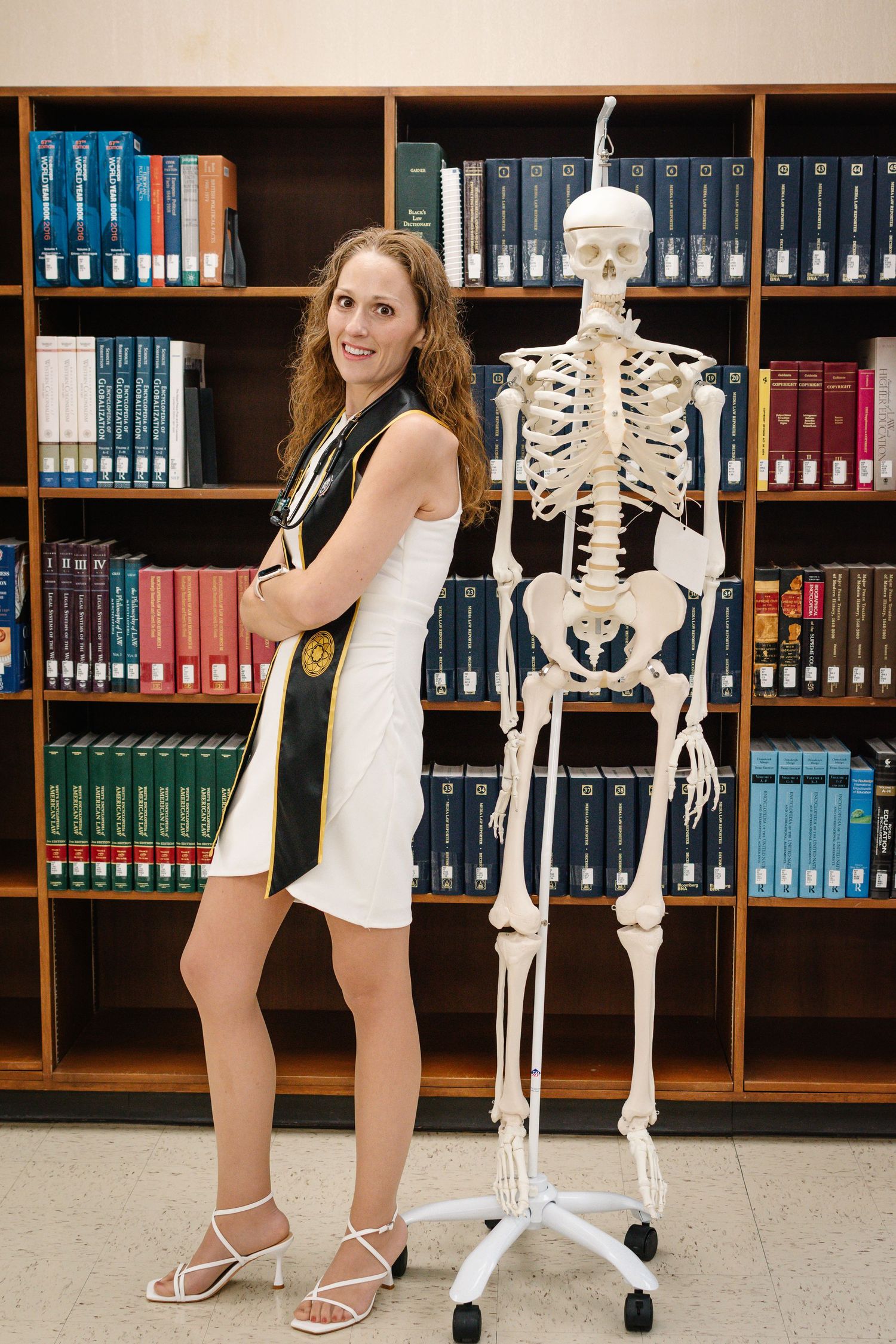 Pacific Lutheran University nursing graduate posing beside skeleton model in library during Tacoma graduation session
