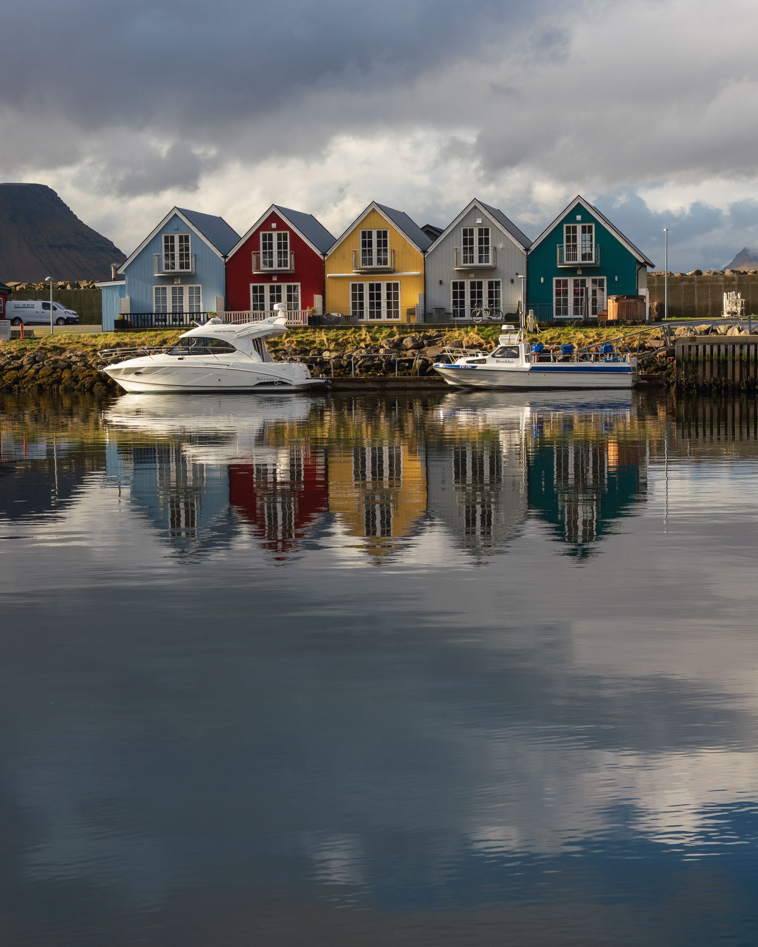 Colorful waterfront houses reflecting in calm harbor waters with boats in foreground.
