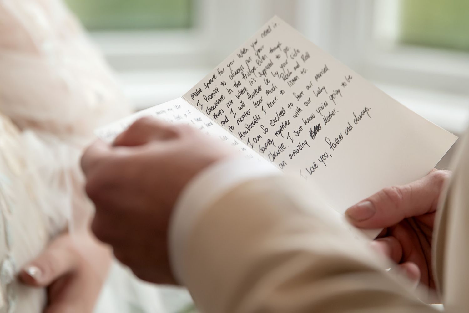 Person in wedding attire reading a handwritten letter, close-up of hands holding a heartfelt note.
