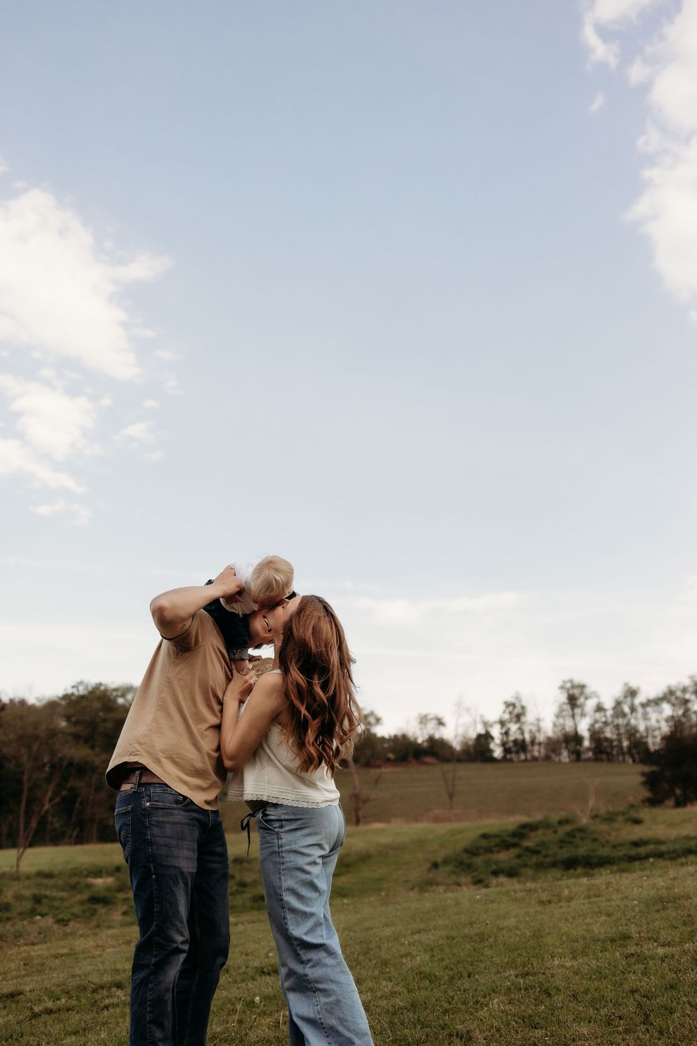 Couple sharing a tender moment outdoors in a lush green field under a cloudy sky.