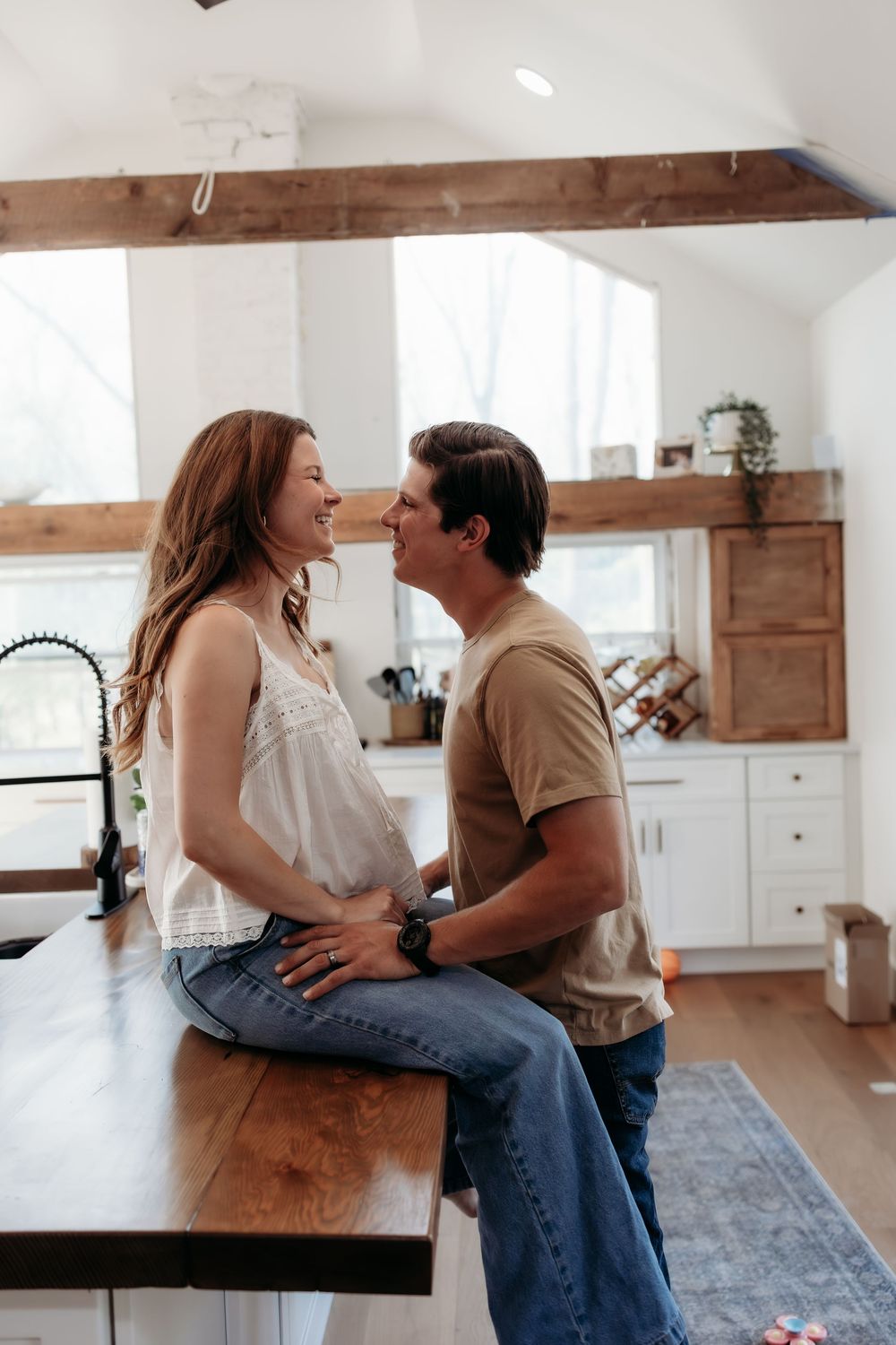 A happy couple shares a romantic moment in a modern farmhouse kitchen, woman sitting on wooden counter.