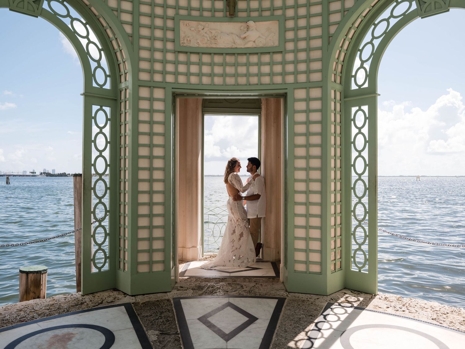 Bride and groom embrace inside Vizcaya’s waterfront pavilion, framed by elegant architecture and sweeping views of Biscayne Bay.
