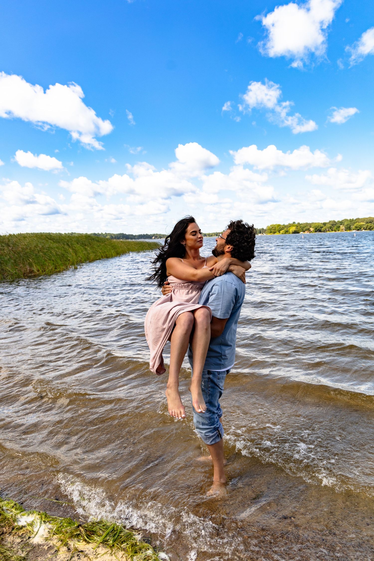 A couple shares a romantic moment as a man lifts a woman in his arms while standing in shallow lake water.