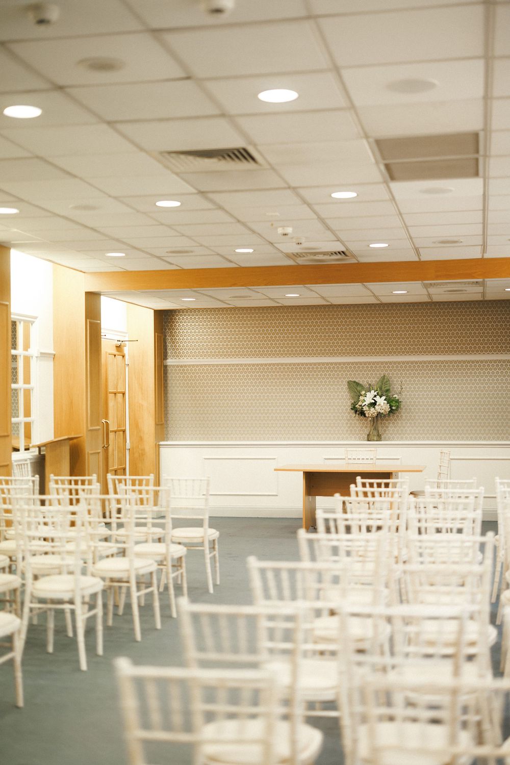 Elegant wedding ceremony venue with white Chiavari chairs arranged in rows facing a floral arrangement on a wooden altar.