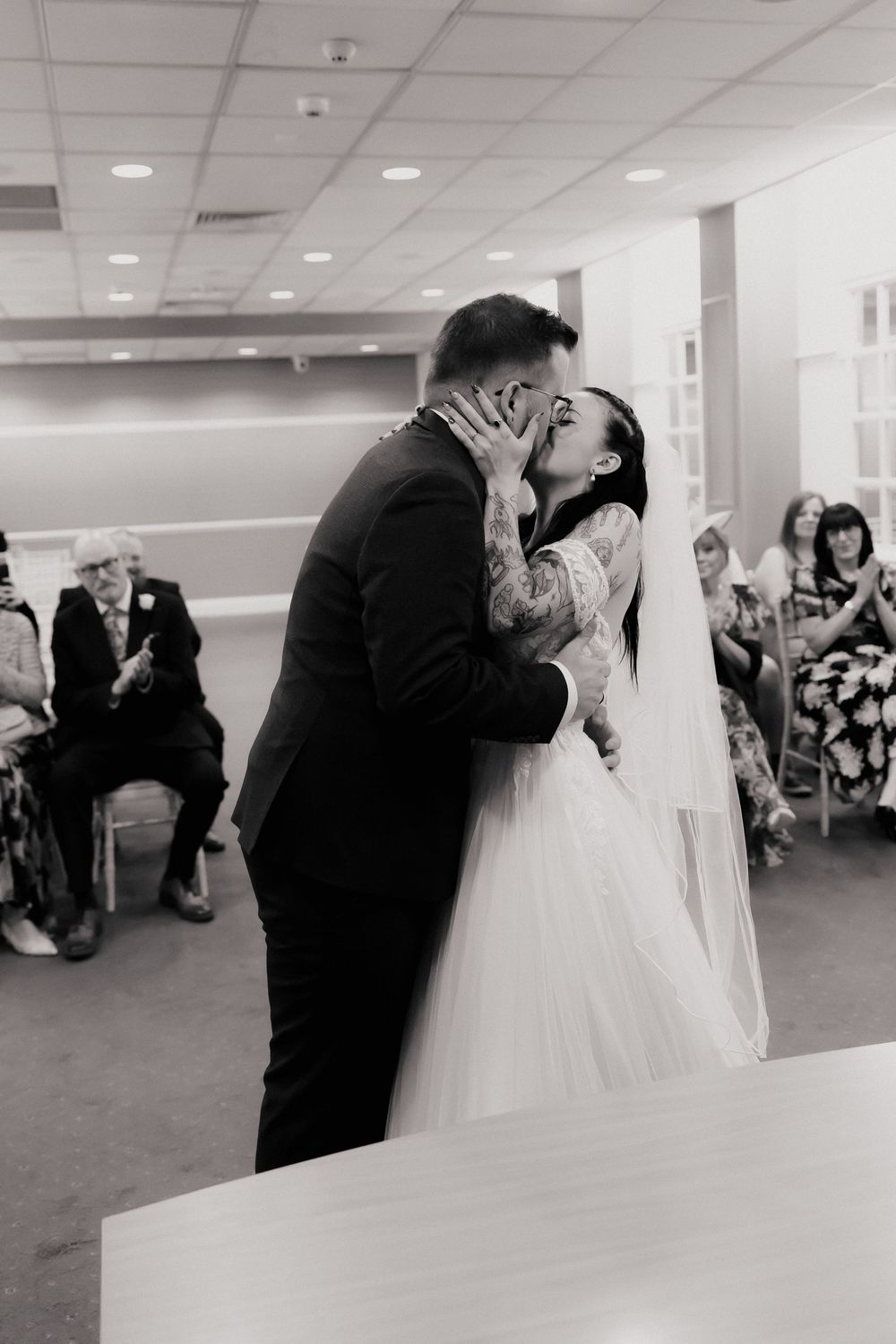 Black and white photo of a bride and groom sharing their first kiss at a wedding ceremony.